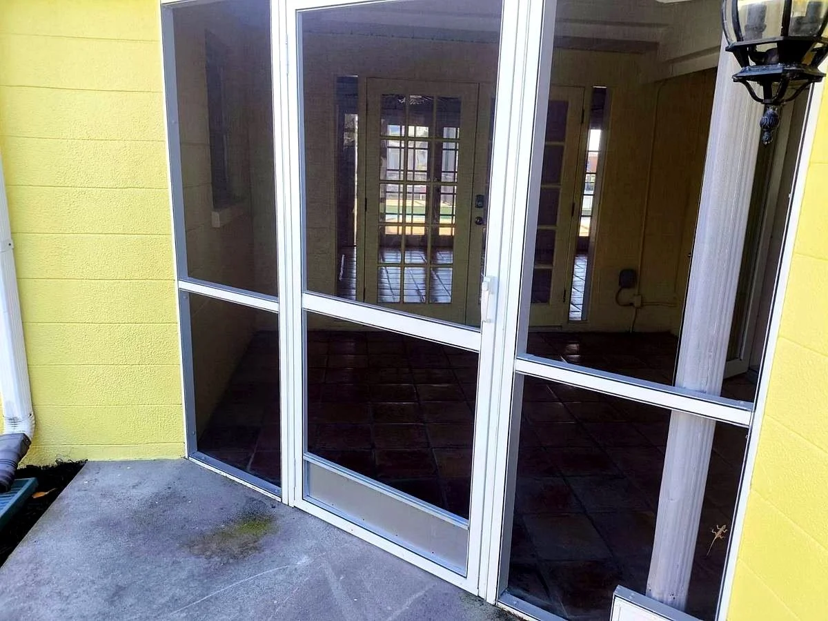 Screened porch entrance with white-framed glass storm doors, yellow exterior walls, tiled floor, and decorative outdoor lantern