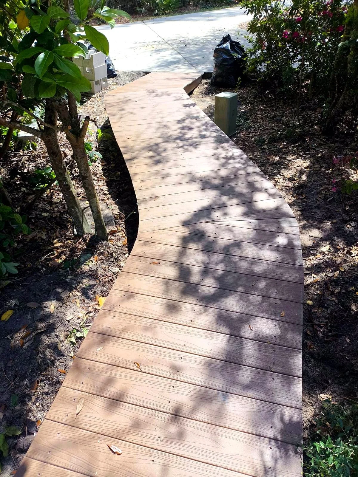 Wooden garden walkway leading through lush landscaping to a concrete driveway