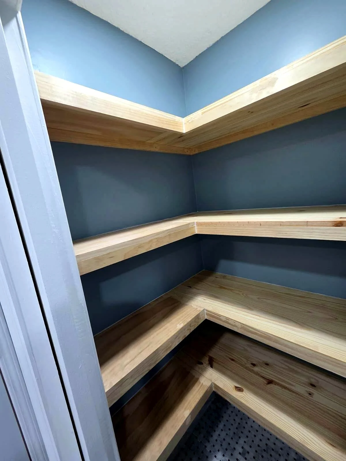 Empty walk-in closet with dark blue walls and wraparound natural wood shelving