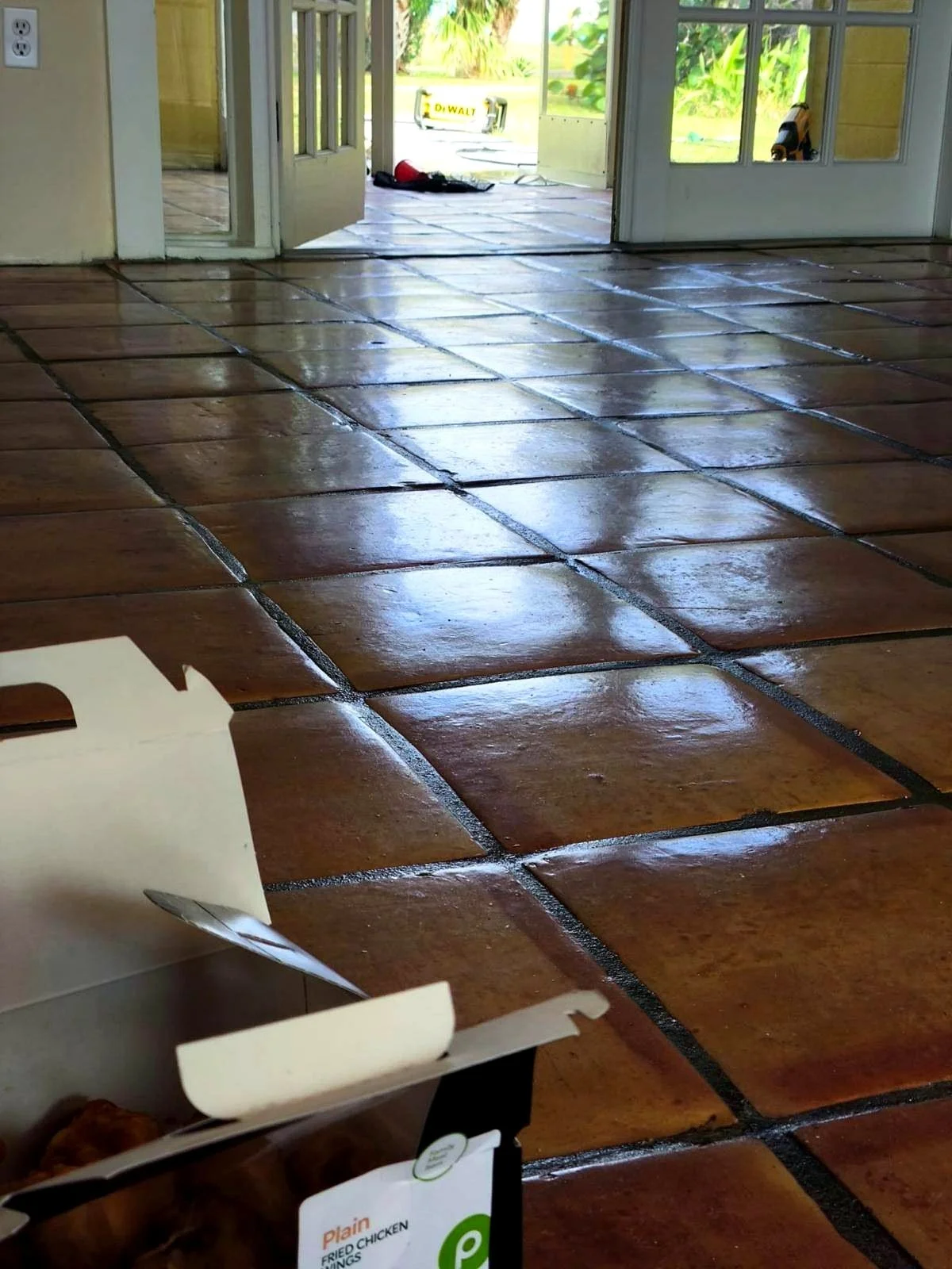 Wet terracotta tile floor inside a home with open doors, construction tools outside.