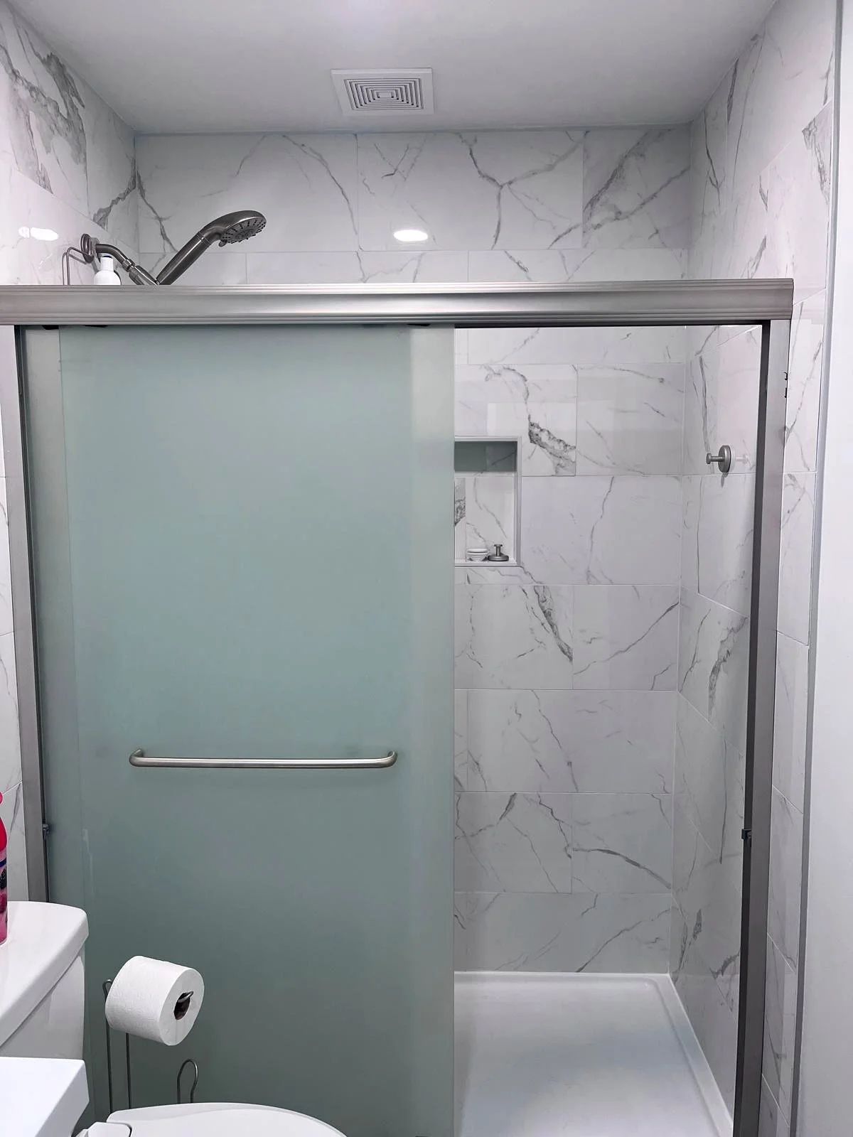 Modern bathroom with marble-patterned tile, frosted glass sliding shower door, handheld showerhead, and white shower base