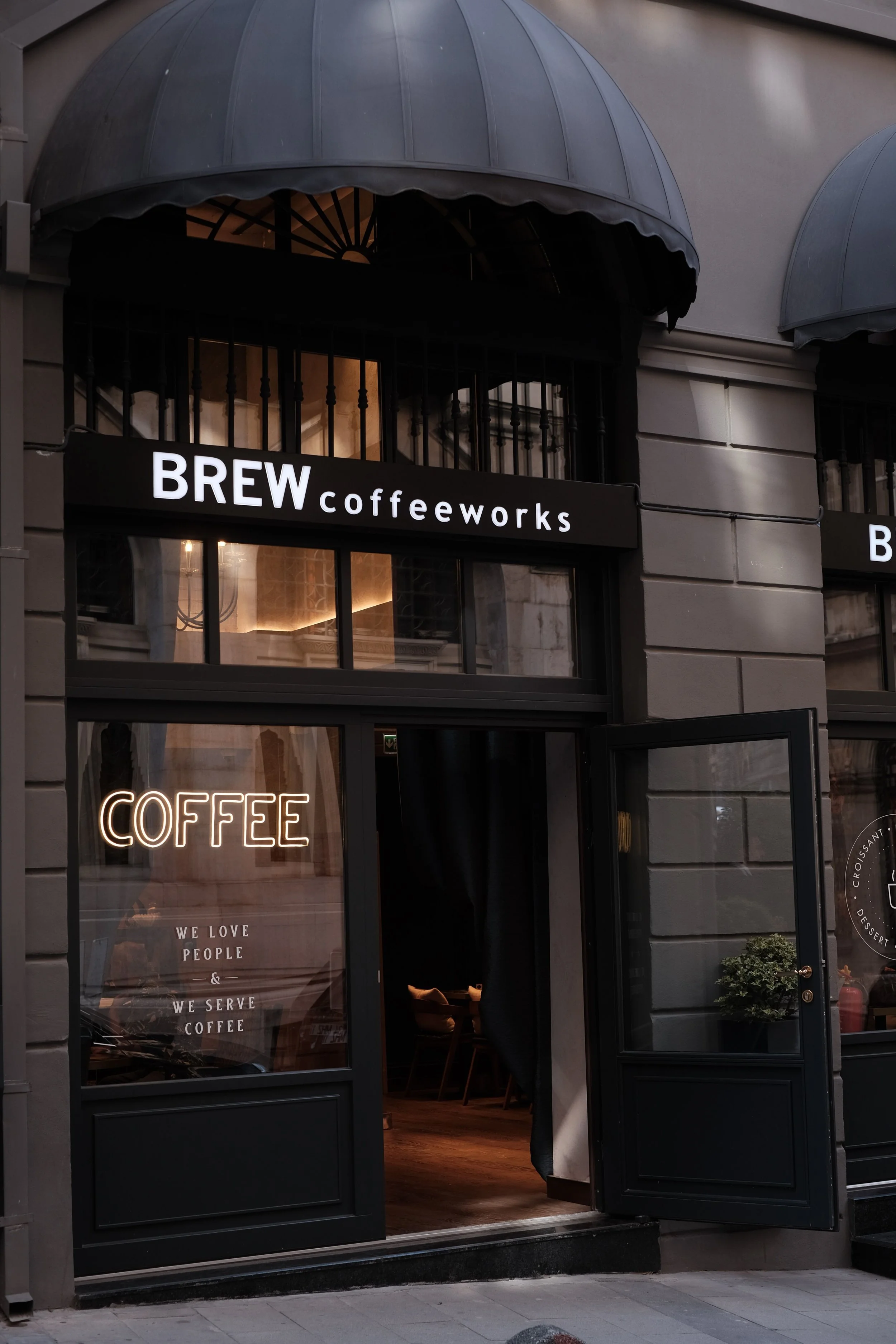 Exterior of BREW Coffeeworks coffee shop with black awning, illuminated coffee sign, and open entrance.
