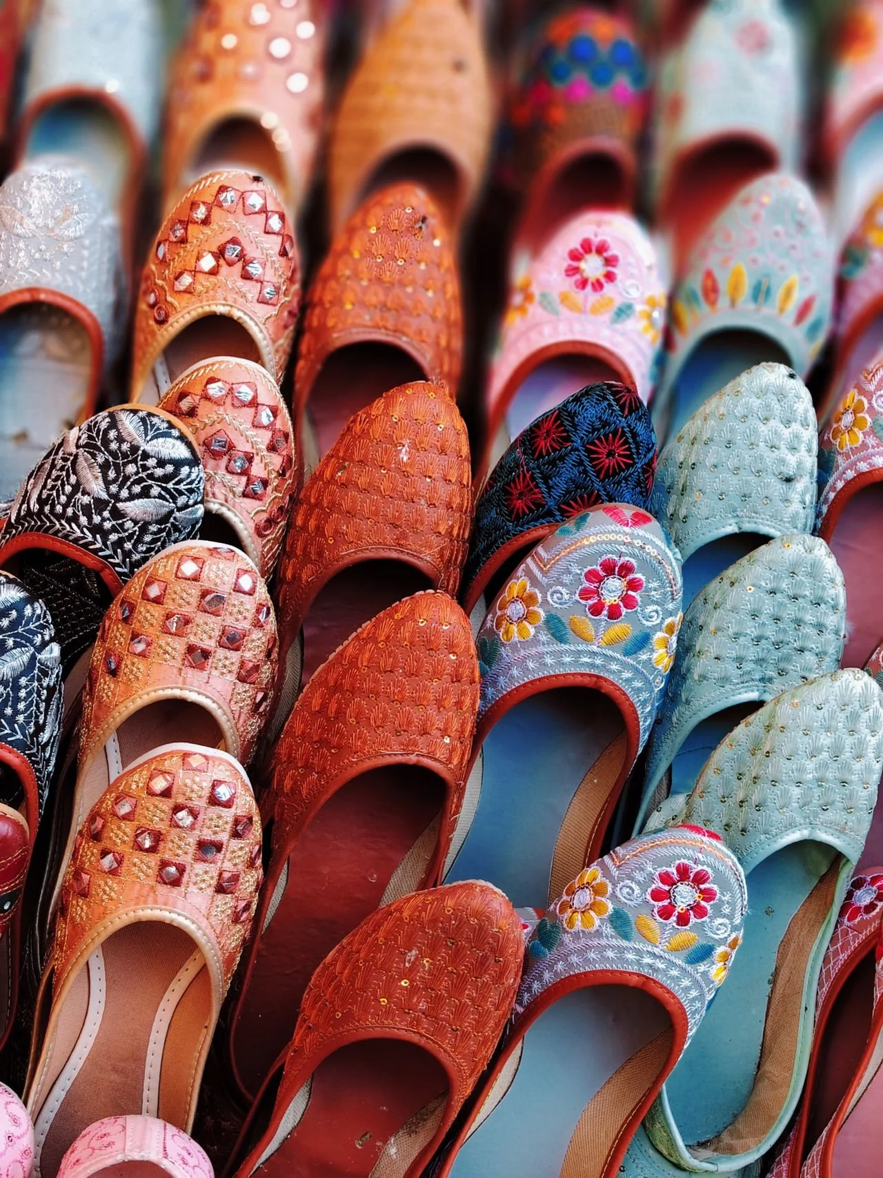 A collection of colorful embroidered or beaded slippers with floral and geometric patterns neatly arranged.