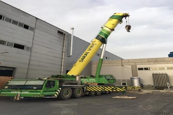 A large green and yellow mobile crane parked outside a commercial building with its boom extended upward.
