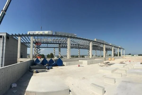 Construction site with a steel framework structure and concrete foundation, and a clear blue sky.