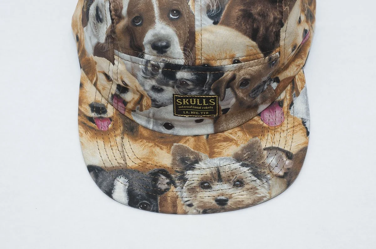A hat with a pattern of various puppy faces and a black label that reads 'Skulls International Rebels LA, NYC, TYO'.