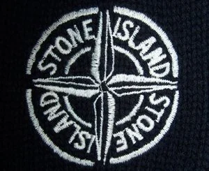 Close-up of Stony Island logo embroidered on black fabric, featuring a circular design with 'Stone Island' text and compass-like emblem.