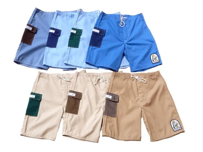 Six pairs of men's swim trunks in various colors: blue, light blue, navy, teal, beige, and tan, with patches on the left leg, some with drawstrings.