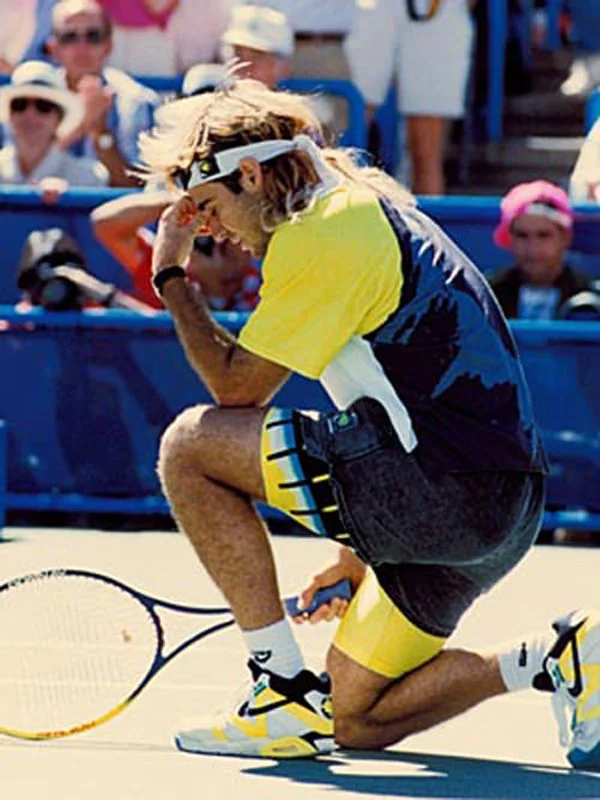 A person dressed in yellow and black sportswear kneeling on a tennis court with a tennis racket, appears to be upset, with spectators watching in the background.