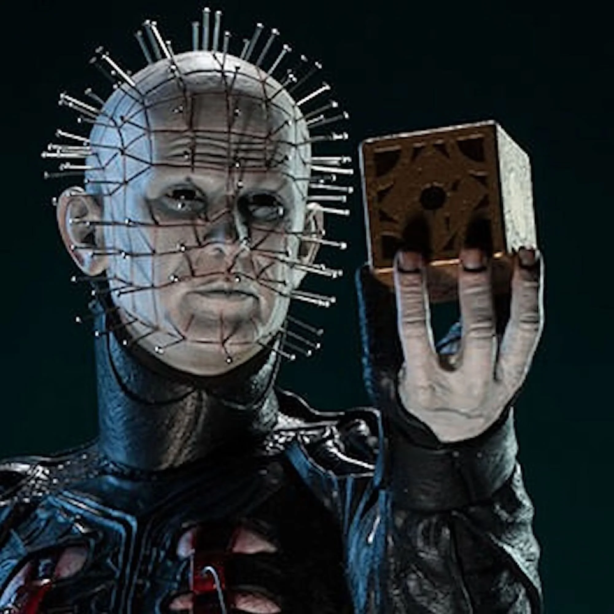 A black-and-white image of a person with face paint resembling a skeleton, wearing a metallic headpiece and intricate costume, holding a small wooden box with carved details, against a dark background.