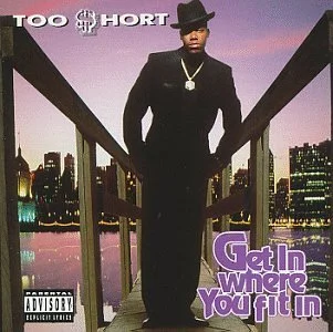 Album cover of Too Short's 'Gettin' Wet & Fit In' featuring a man in a black suit and hat walking on a bridge with a city skyline in the background.