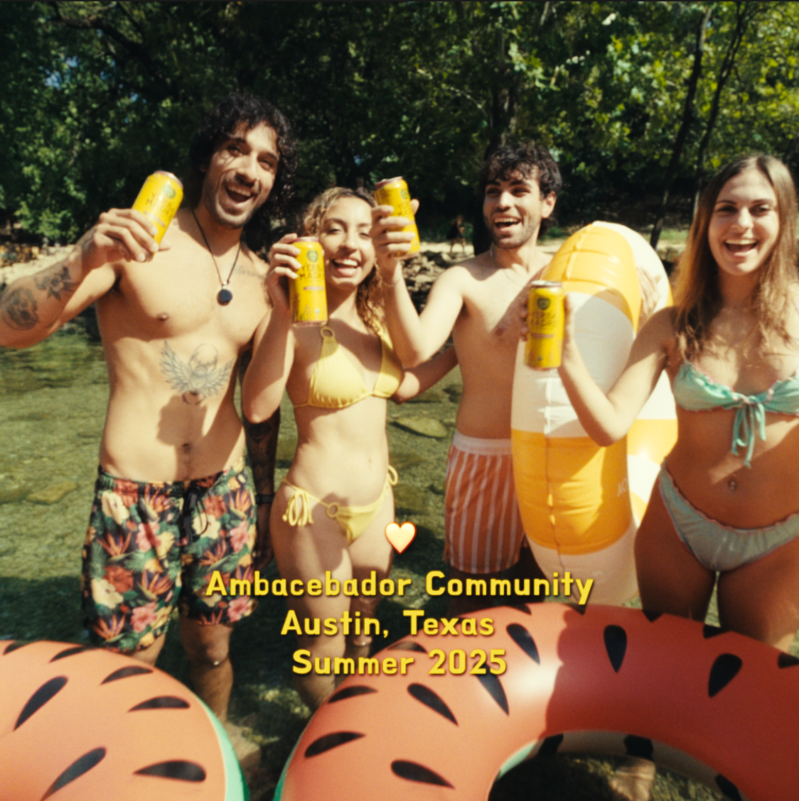 Group of four young adults in swimsuits enjoying a summer day in a river with inflatable floaties, holding drinks and smiling at the camera, surrounded by trees, with text overlay saying 'Ambacebador Community Austin, Texas Summer 2025'.