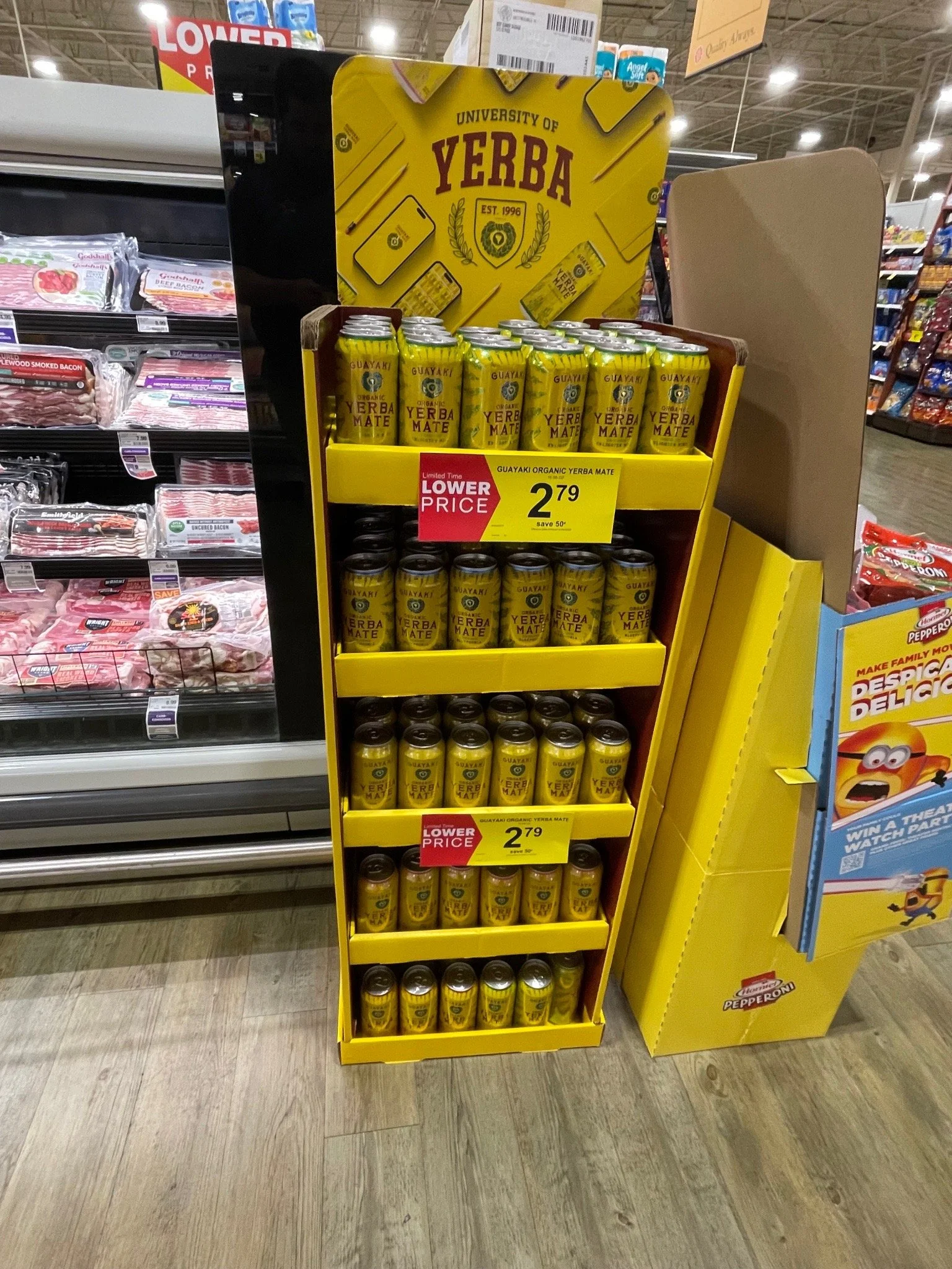 Shelf display of Guayaki Organic Yerba Mate cans in a supermarket. The cans are yellow with red and green text. A sign indicates the price as $2.79.