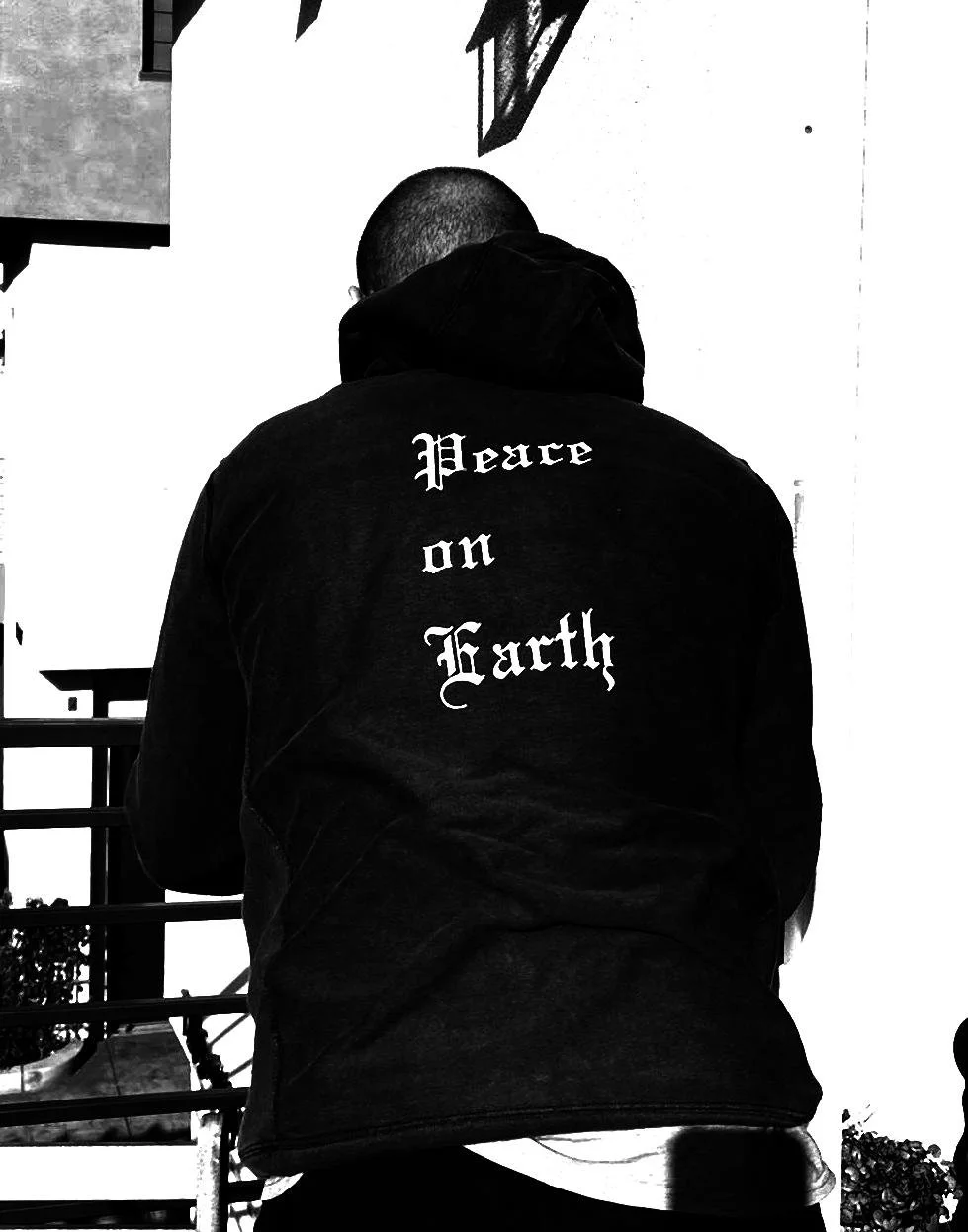 Back view of a person wearing a black jacket with the words 'Peace on Earth' printed on the back, standing outdoors near a building.
