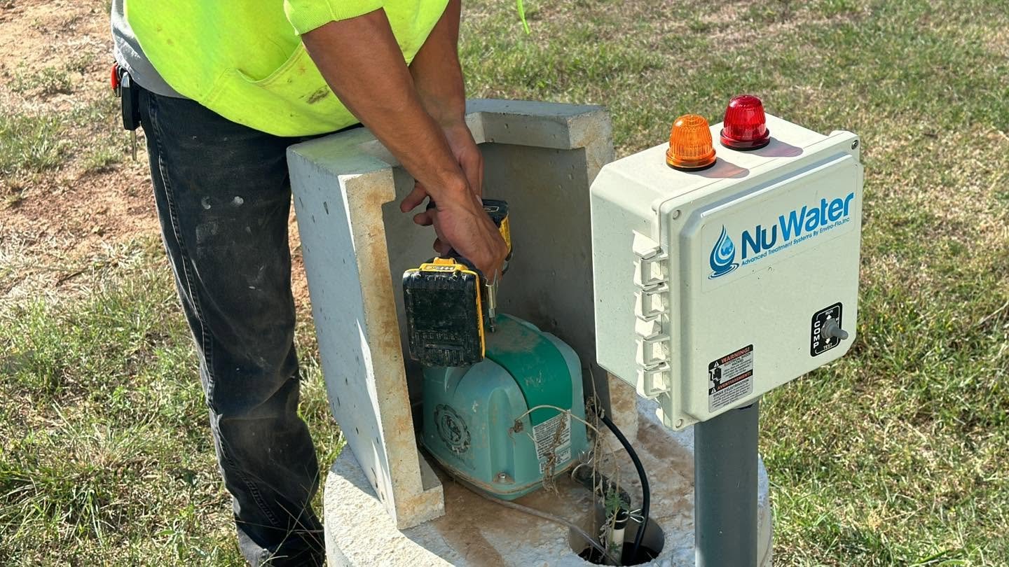Worker installing or maintaining water treatment equipment outdoors, wearing a yellow safety vest, with a NuWater control box and a motor inside a concrete or metal structure.