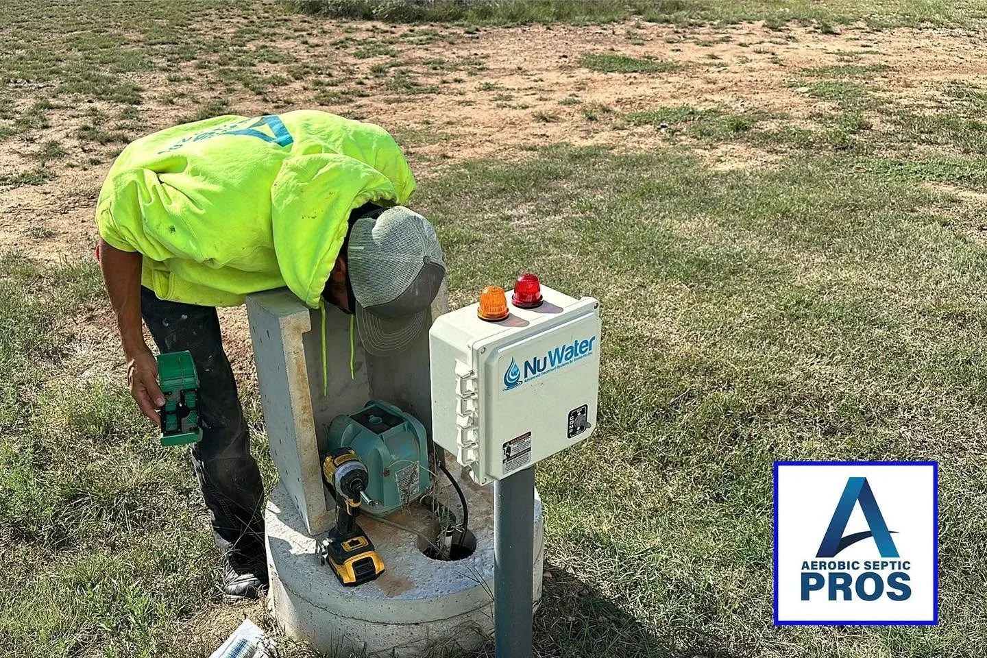 A person inspecting a septic system with equipment, wearing a yellow hoodie and gray cap, in an open grassy area.