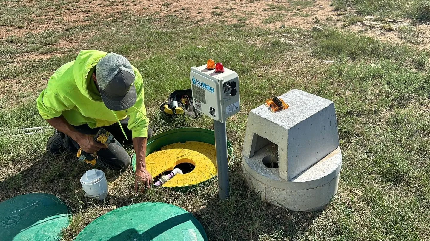 Technician installing a water monitoring device in a grassy outdoor area with equipment and tools around.