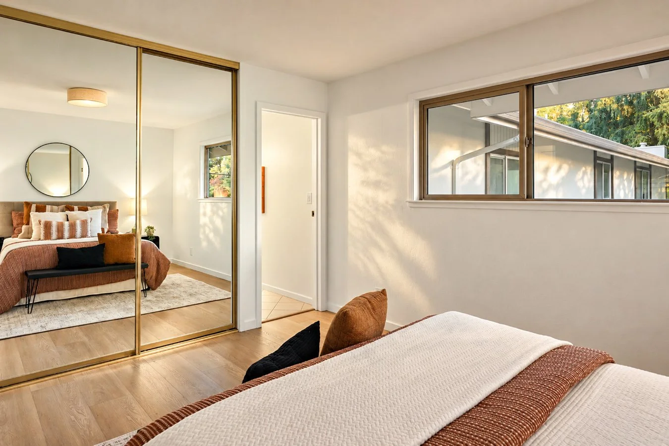 Bedroom with a bed, pillows, a mirrored closet, and a large window showing trees outside.