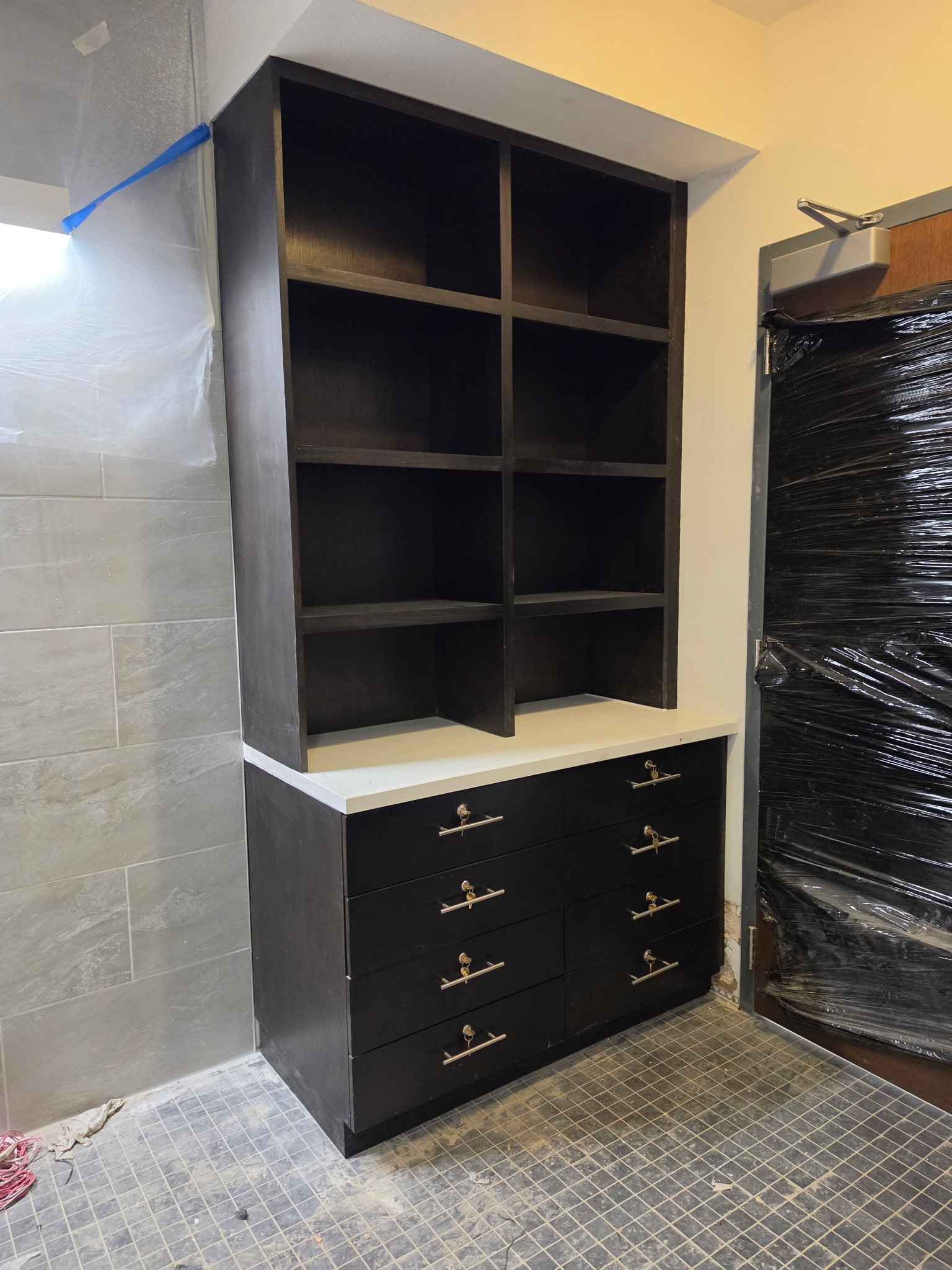 Black kitchen cabinet with multiple drawers and open shelving, partially installed in a room under construction or renovation.