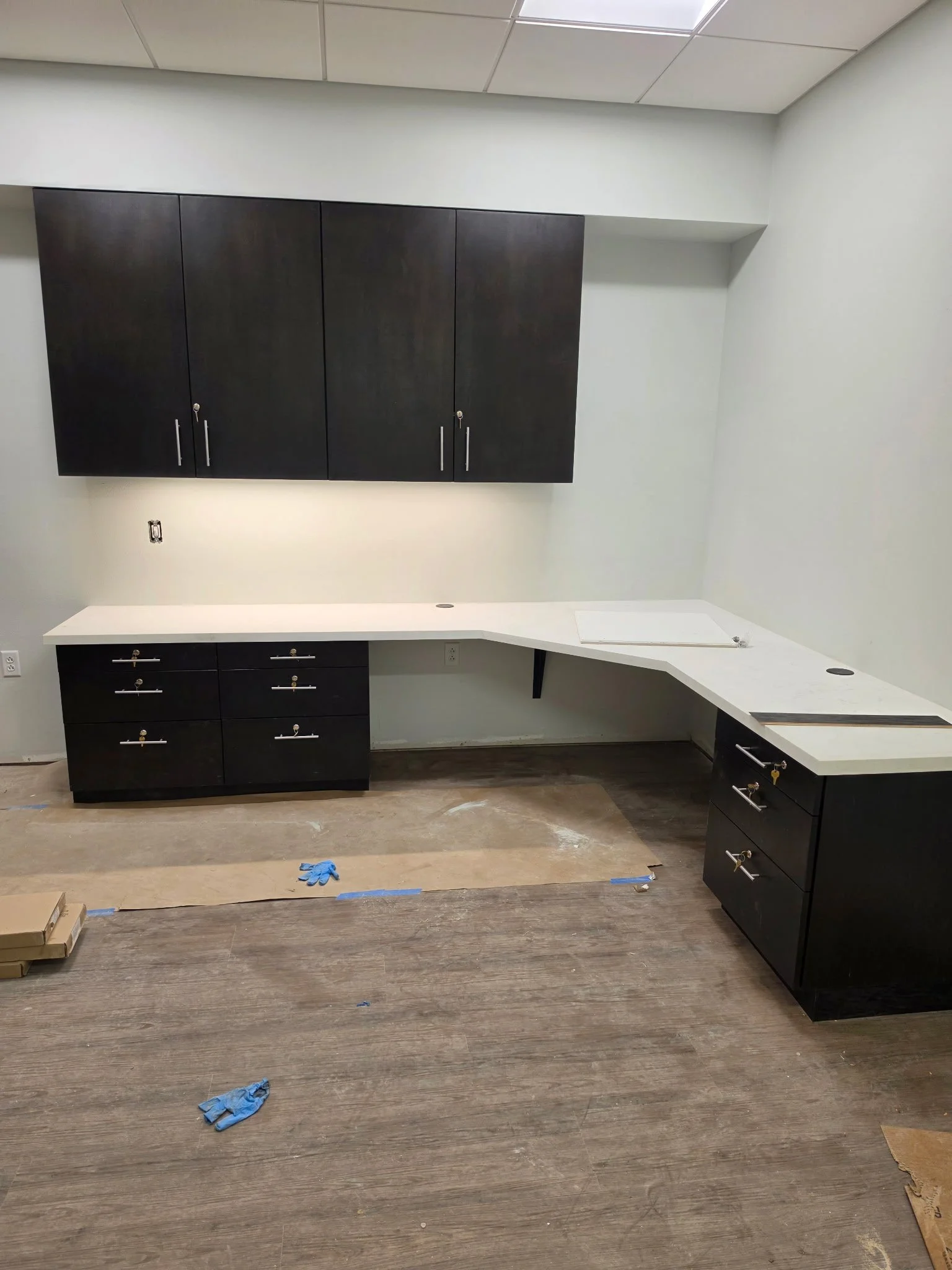 Room under construction or renovation with black cabinets, white countertop, and scattered blue gloves on a wooden floor.
