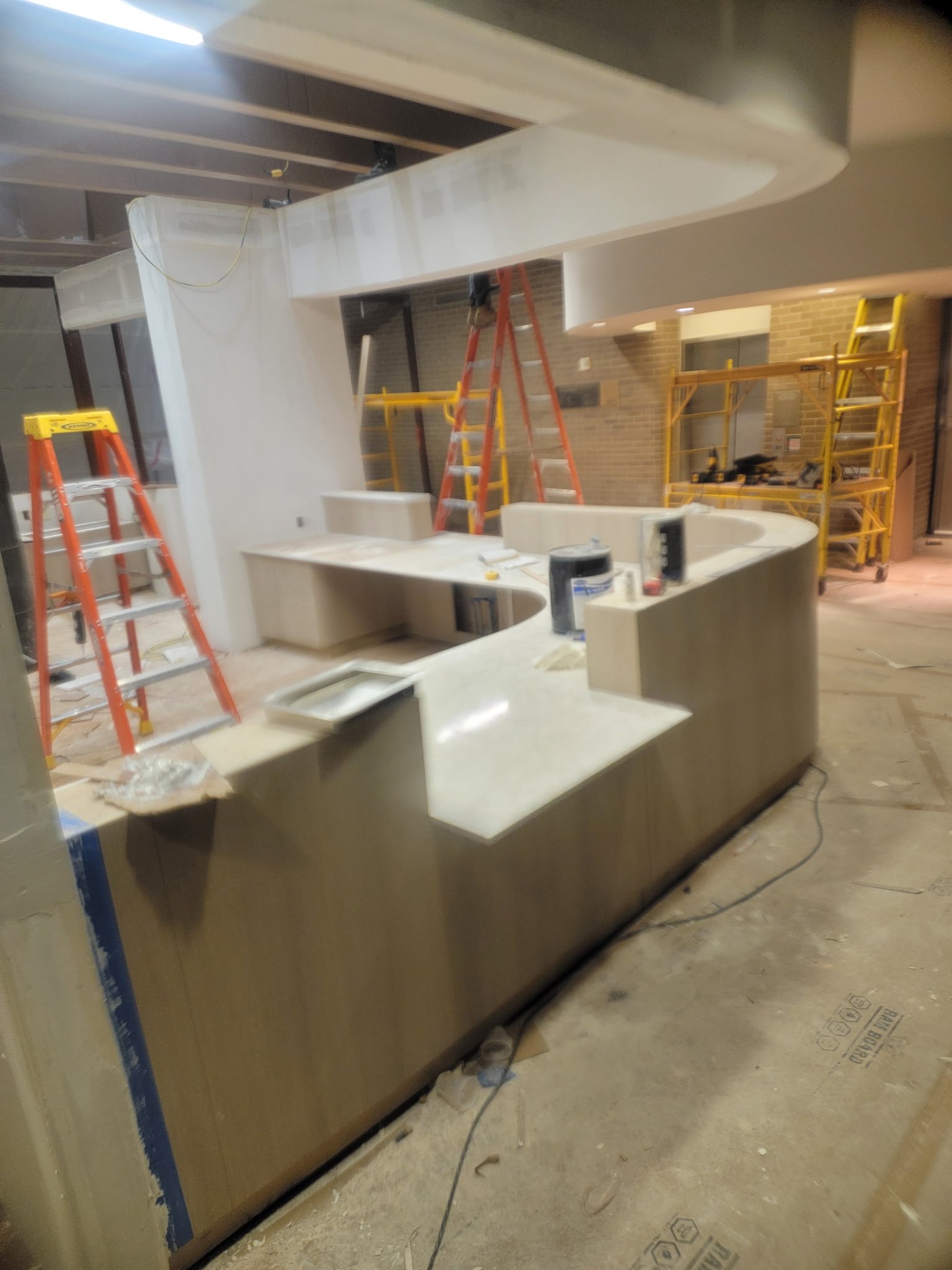 Interior of a construction site with unfinished drywall, ladders, scaffolding, and tools for building or renovating a space.