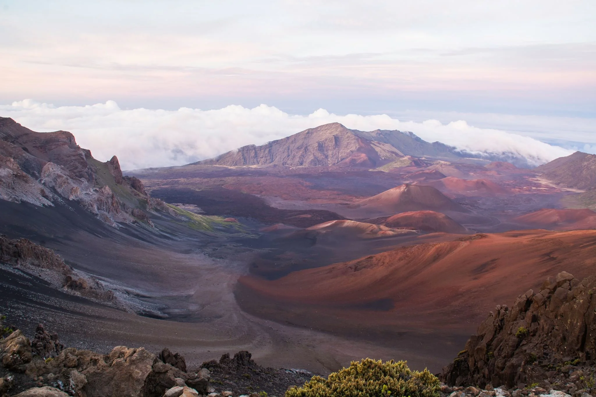 Scenic landscape of volcanic mountains with rocky terrain, sagebrush, and clouds in the background during sunset.