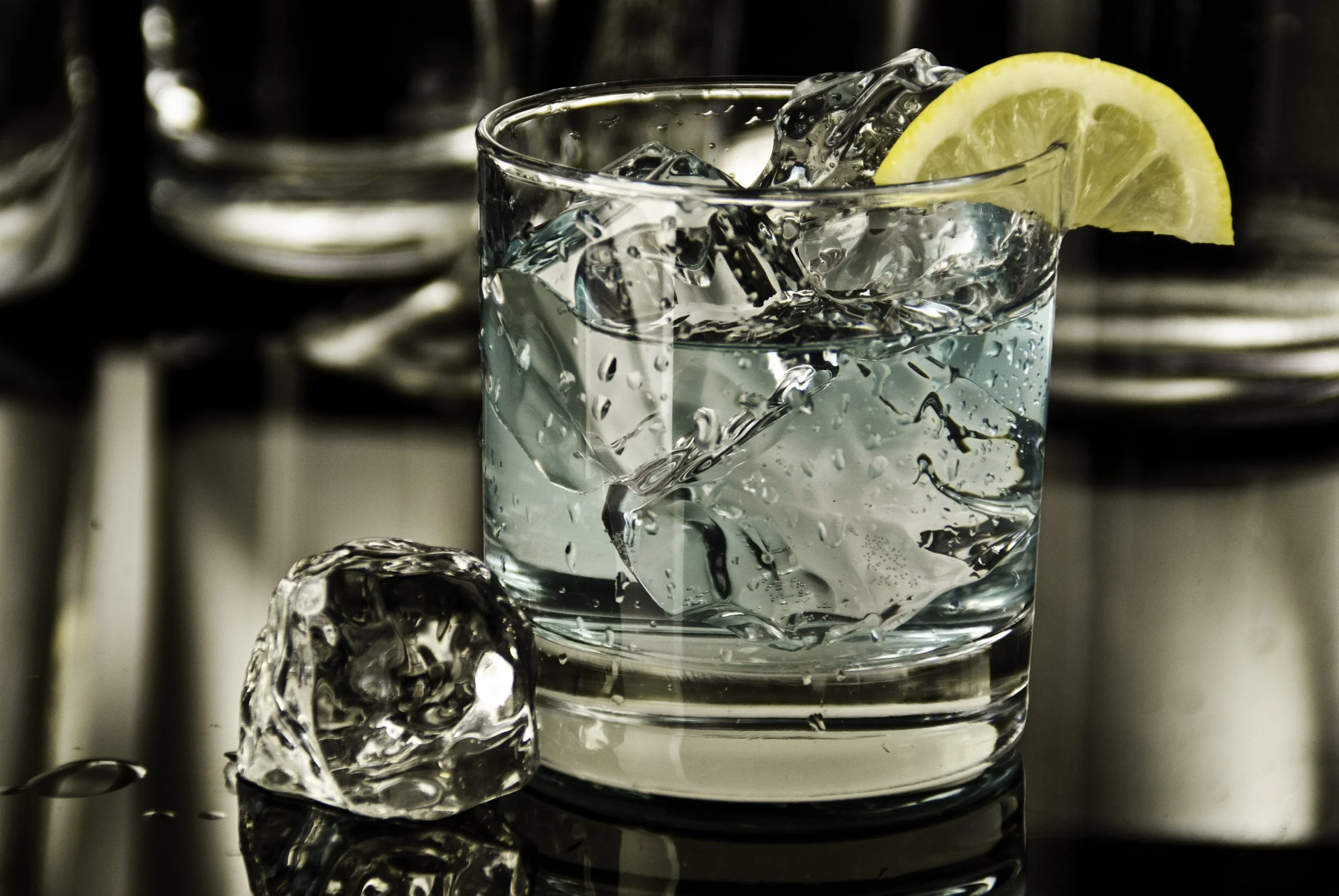 A glass of water with ice cubes and a lemon wedge garnishment.
