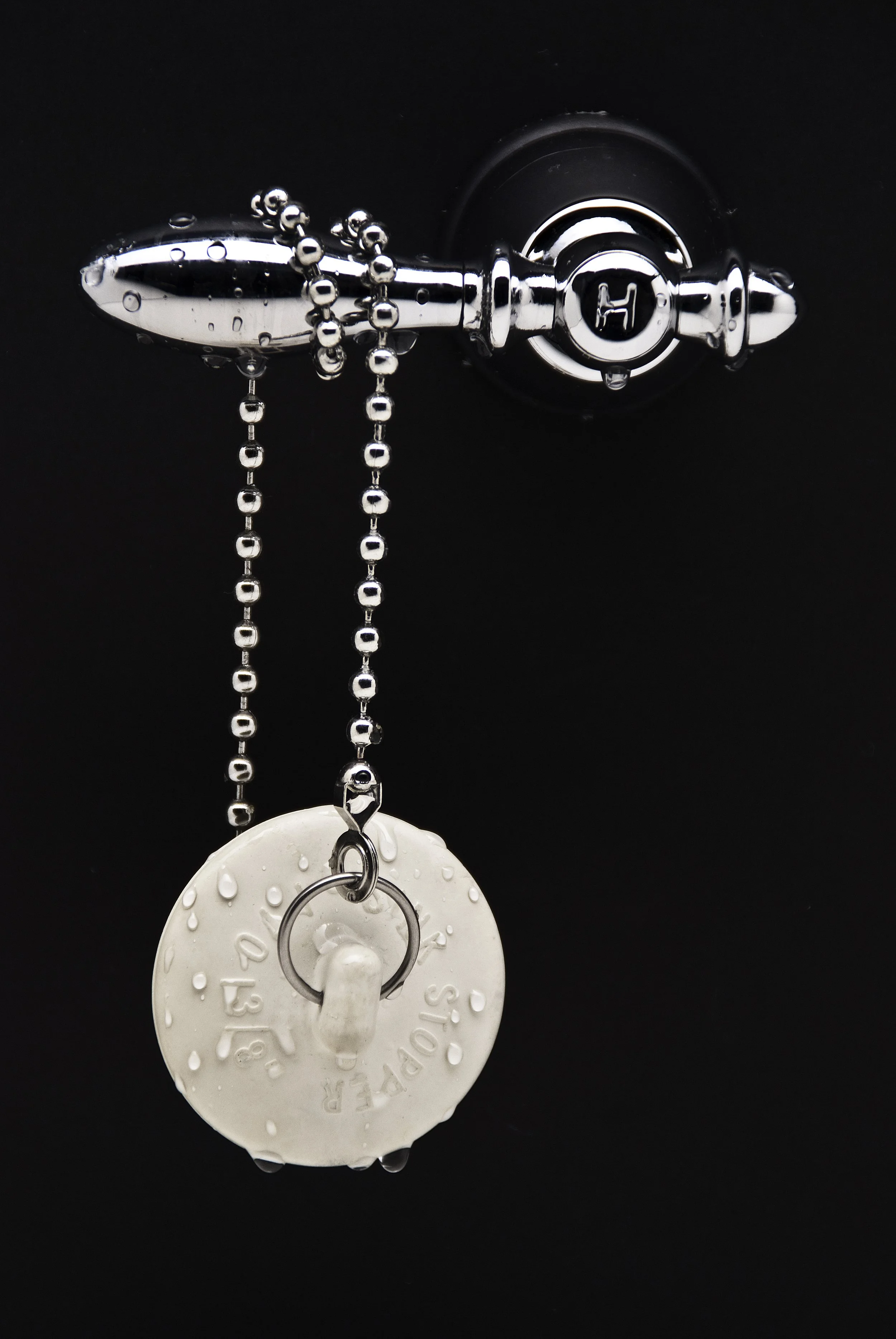 Close-up of a silver door handle with a keychain and water droplets on it, mounted on a dark surface.