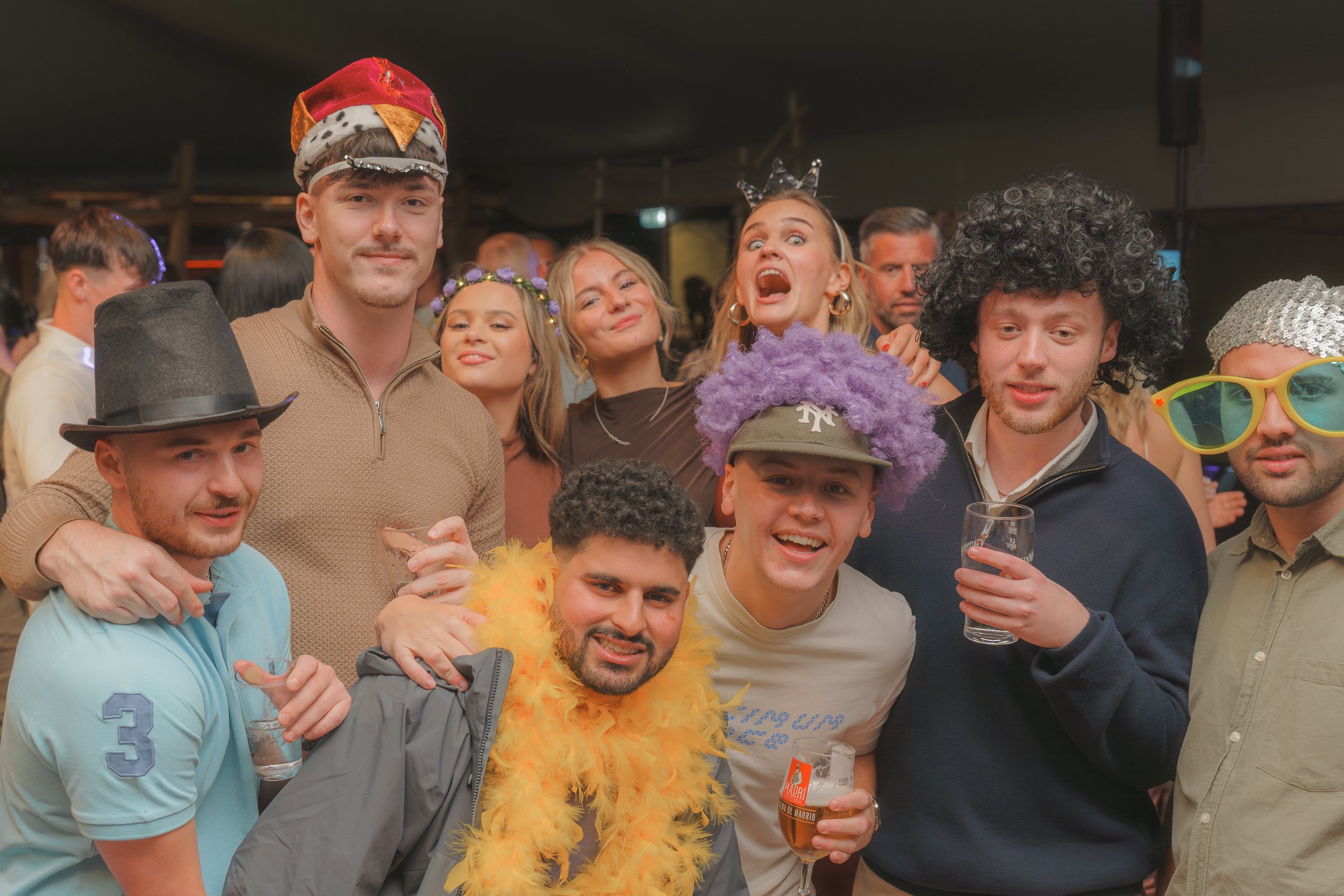 Group of people in costumes and accessories celebrating at a party, some holding drinks.
