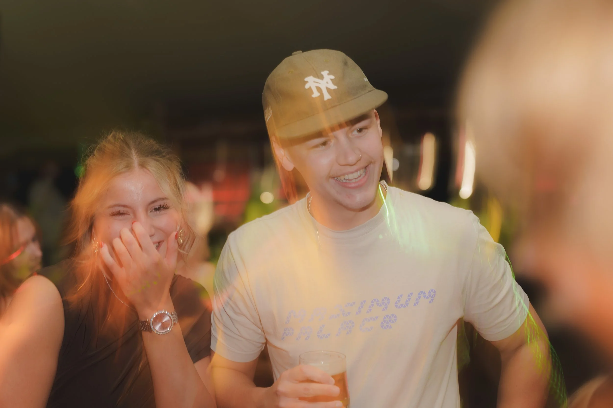 A group of young people enjoying themselves at a party or social gathering, with one person holding a drink and smiling.