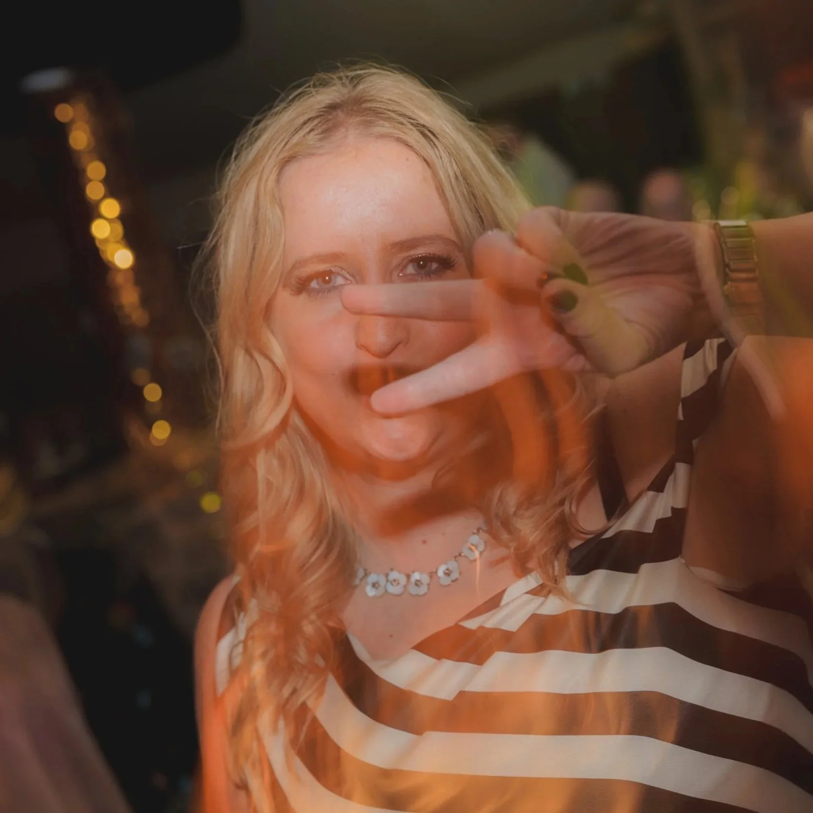 A woman with blonde hair making a peace sign with her fingers in front of her face.