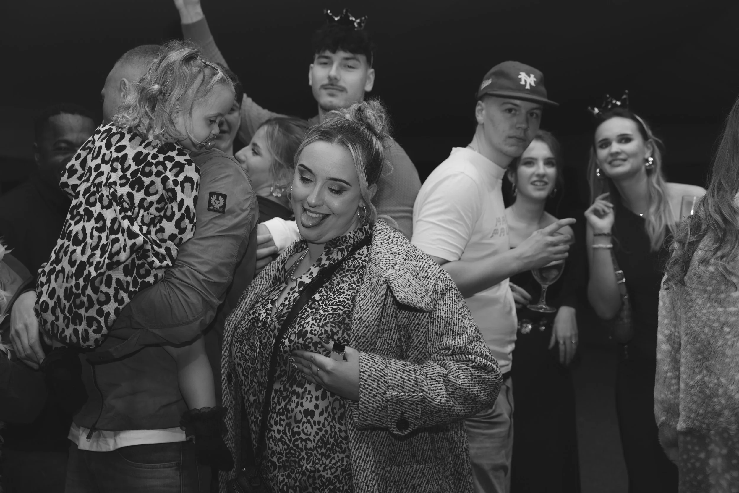 Group of young adults at a party or celebration, some wearing party hats and animal print clothing, socializing and enjoying drinks.