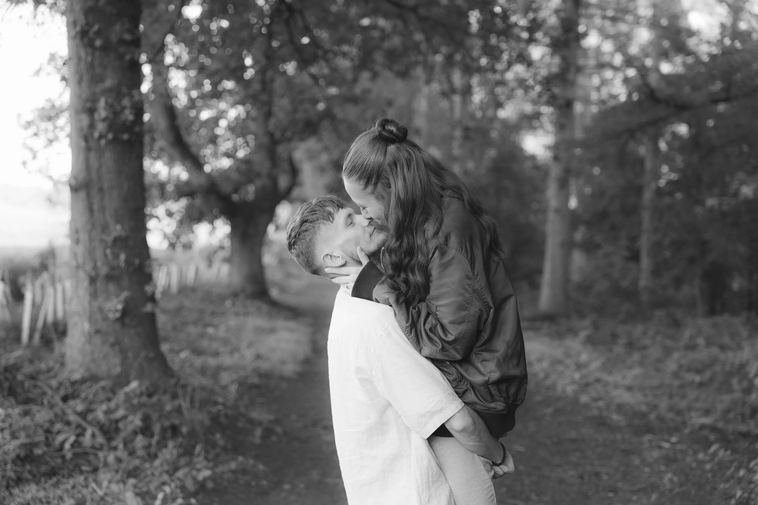 A couple sharing a kiss outdoors in a park, with trees in the background