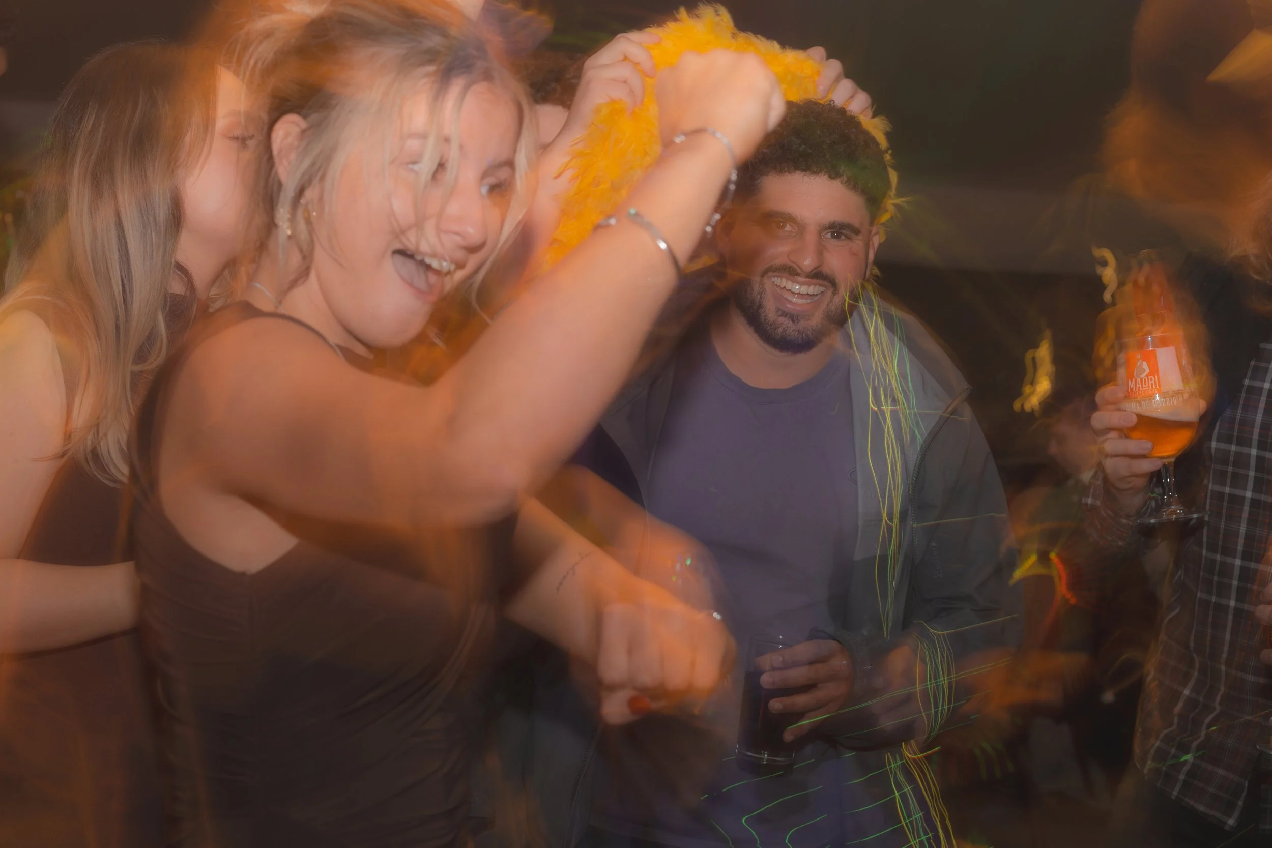 People celebrating at a party with colorful decorations, smiling, and holding drinks, with a lively and joyful atmosphere.