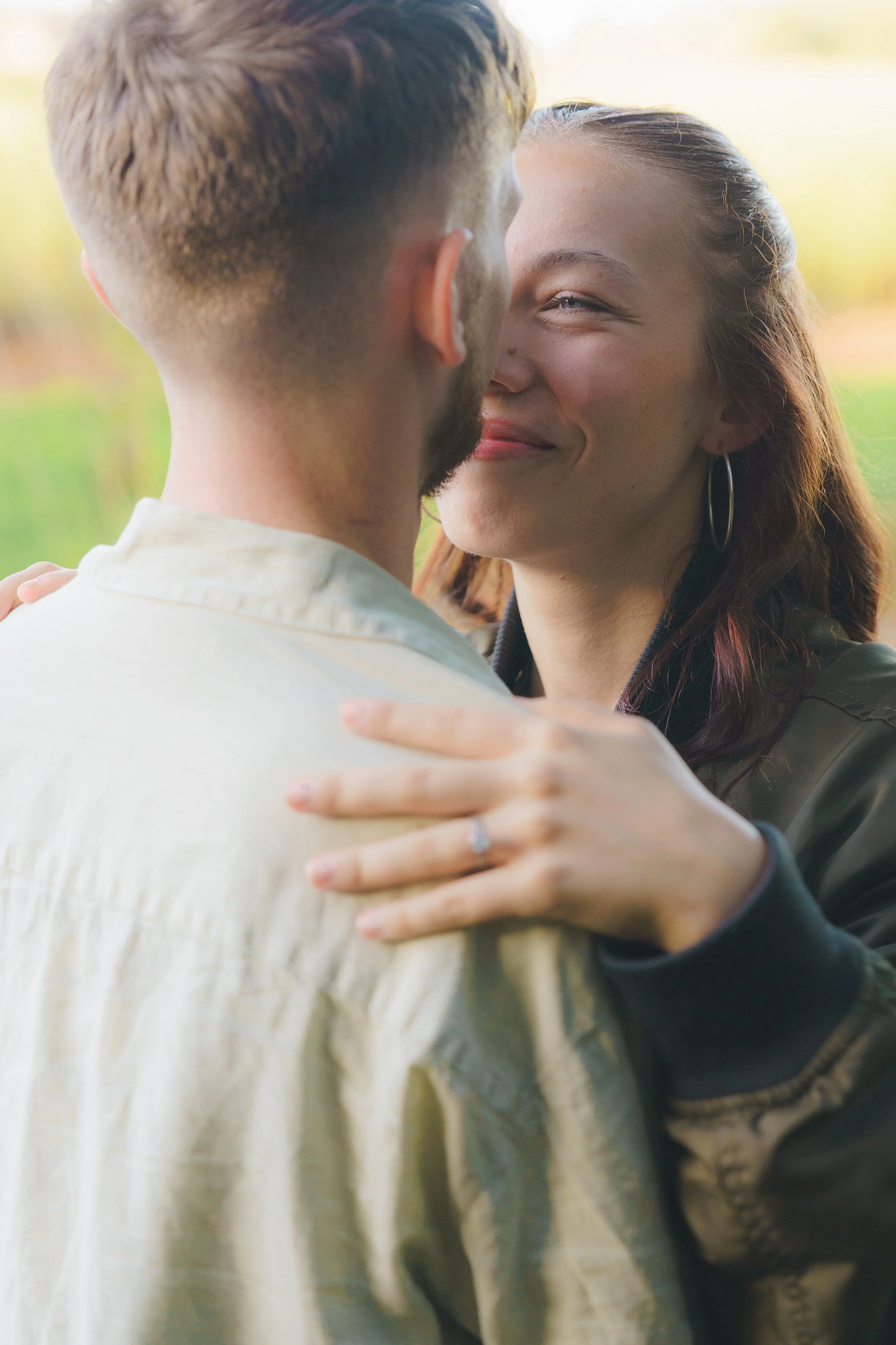 A couple dancing outdoors, close-up shot of their upper bodies, the woman smiling with her hand on the man's shoulder, in a natural setting with blurred greenery background.