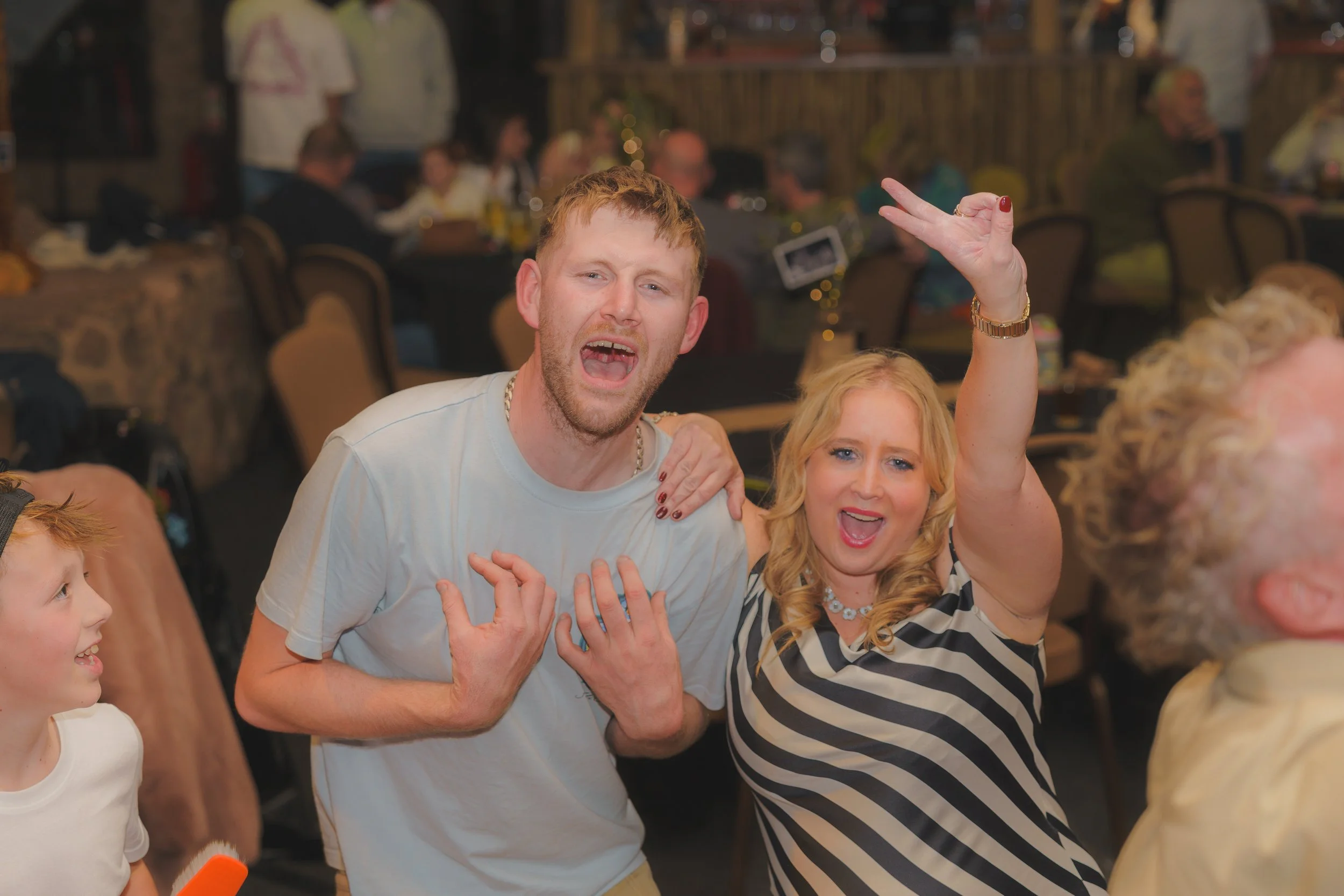 People celebrating at a party, smiling and dancing, with a man and woman in the center showing excitement and joy.