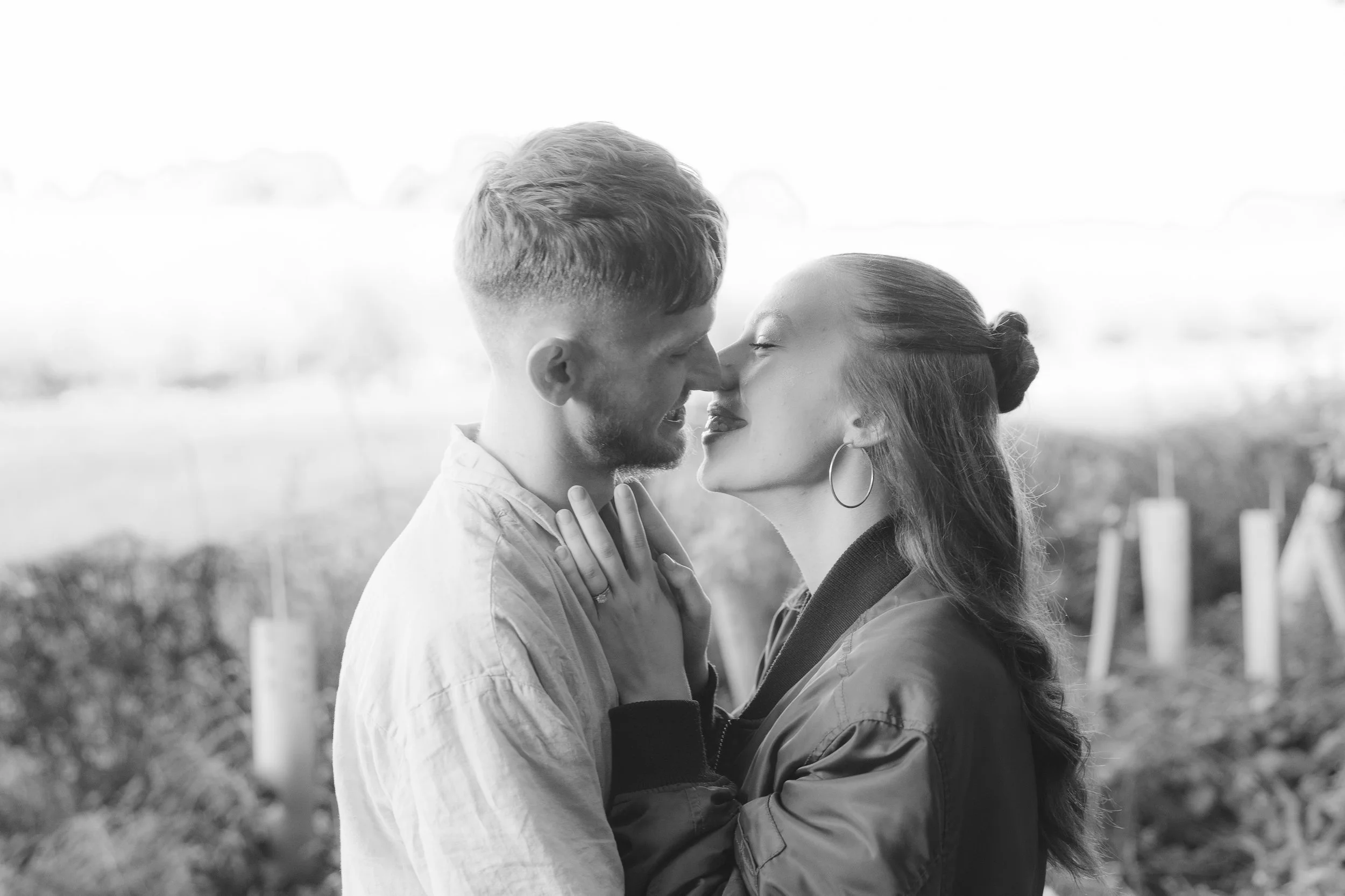 A couple sharing a kiss outdoors, facing each other closely, with a blurred natural background.