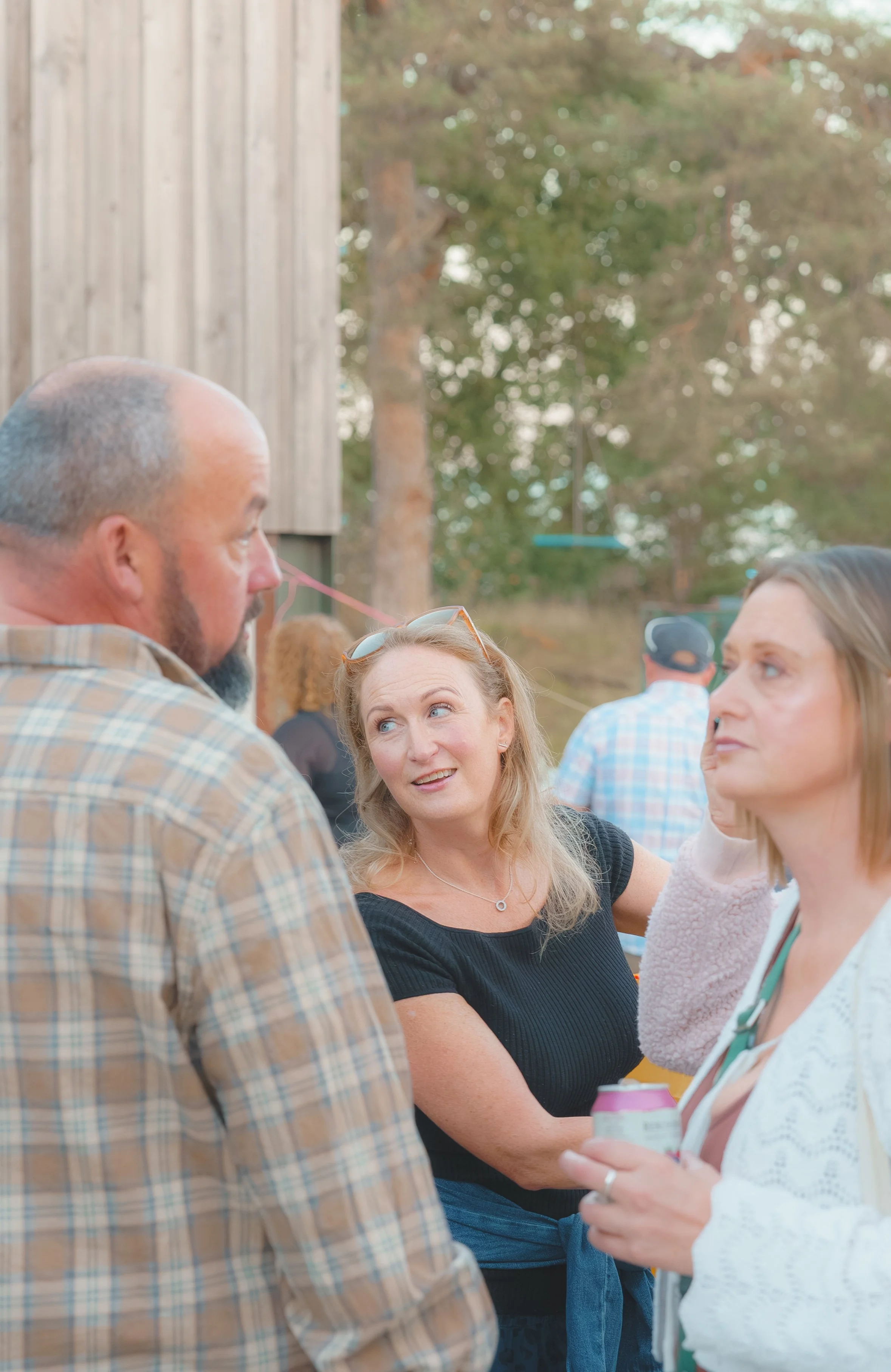 People engaged in conversation at an outdoor gathering during daytime with trees in the background.