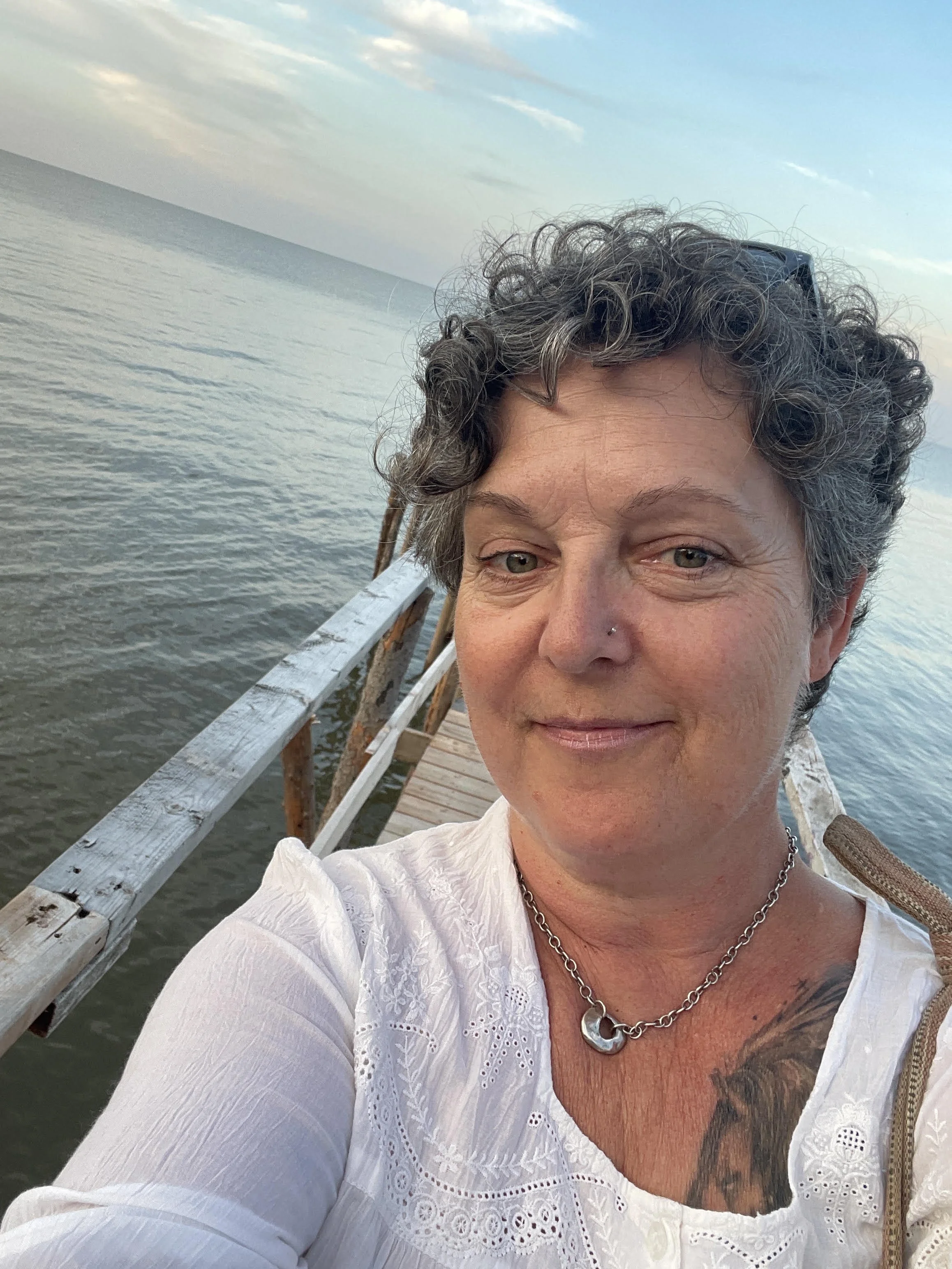 Sherri smiling and sitting on a pier by  Lake Winnipegrt, wearing a green outfit.