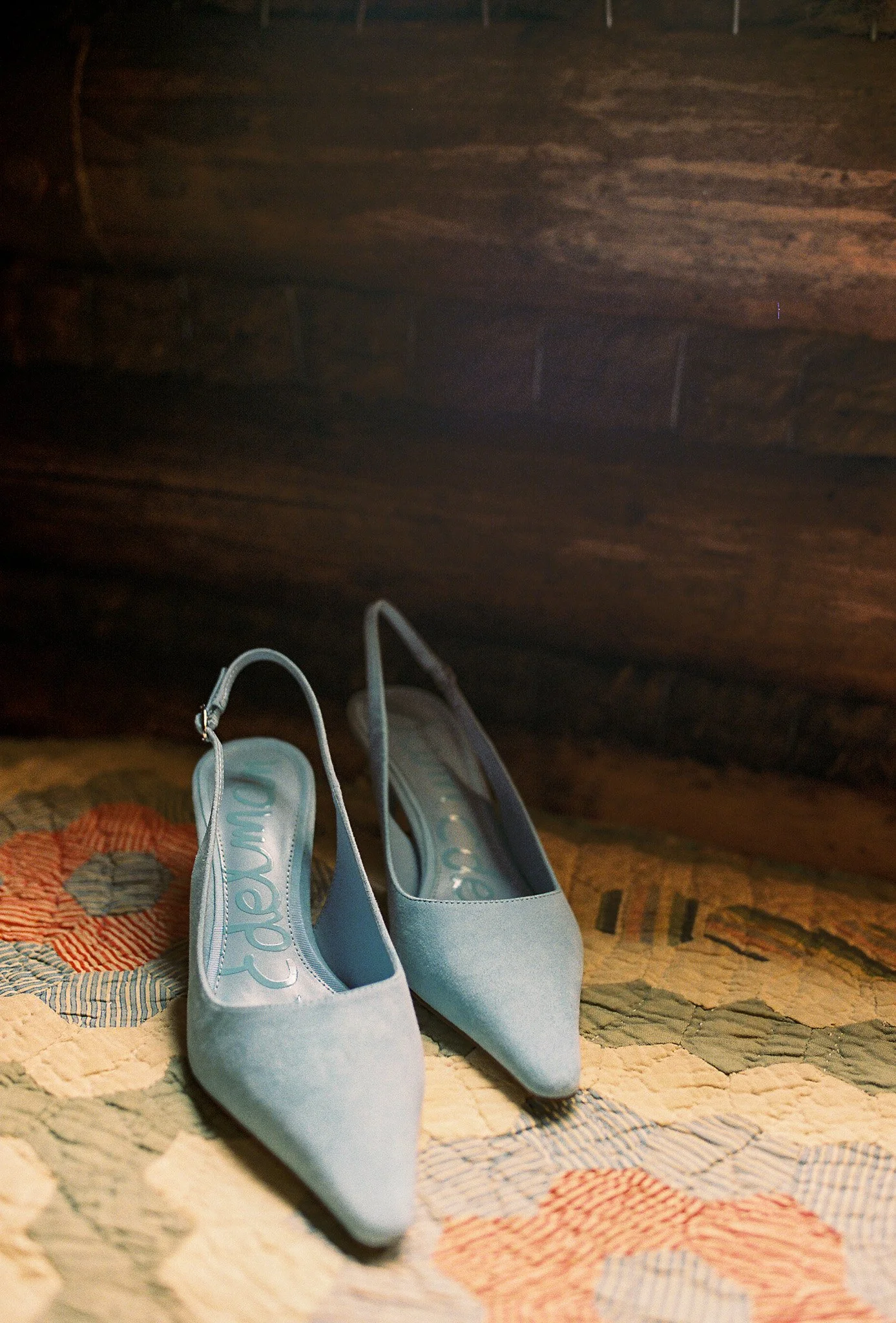 Pair of light blue high-heeled shoes placed on a colorful quilted blanket.