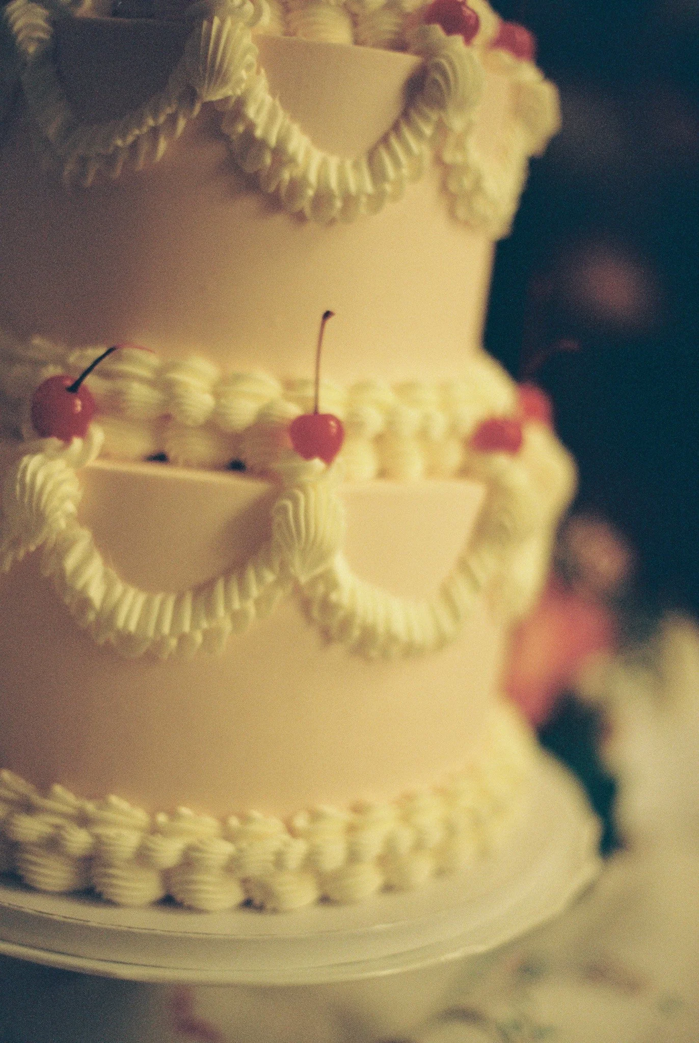 Close-up of a multi-tiered wedding cake decorated with white icing and red cherries.