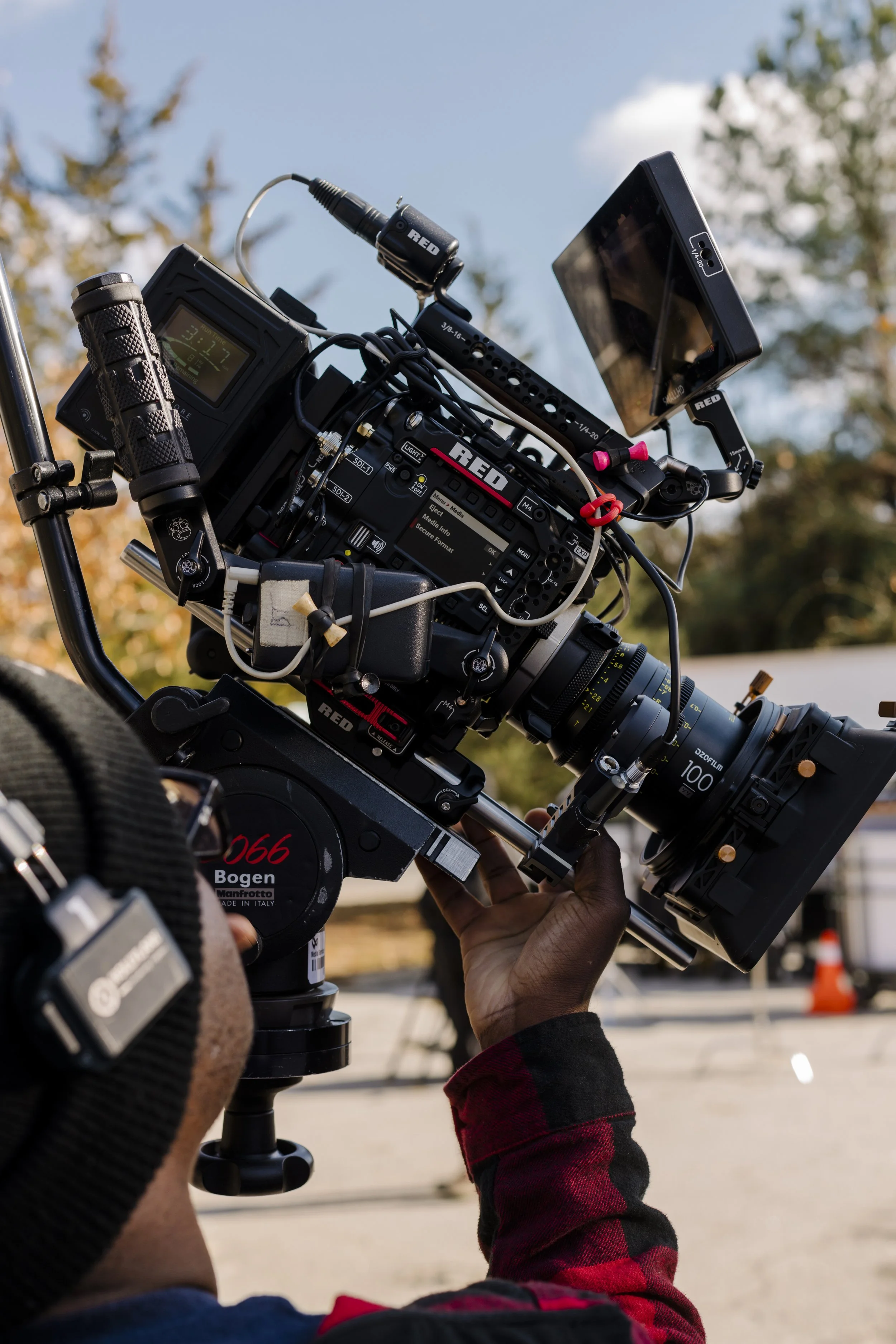 Close-up of a professional RED cinema camera rig with monitor, microphone, cables, and lens outdoors