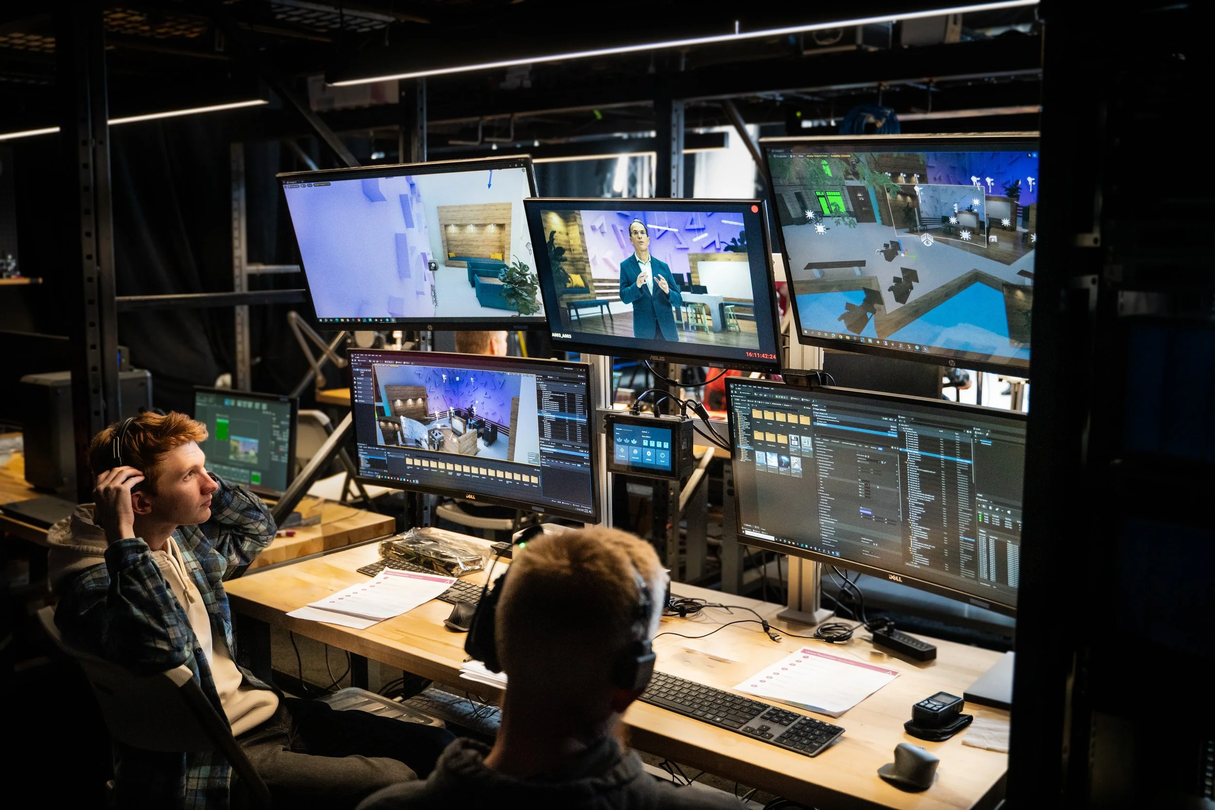 Film production control room with crew members monitoring multiple screens showing a presenter, virtual sets, and computer graphics.