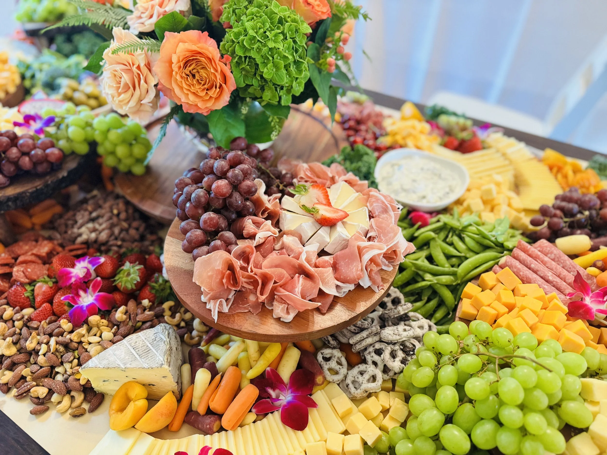 Charcuterie board with prosciutto, cheeses, pretzels, grapes and fresh flowers