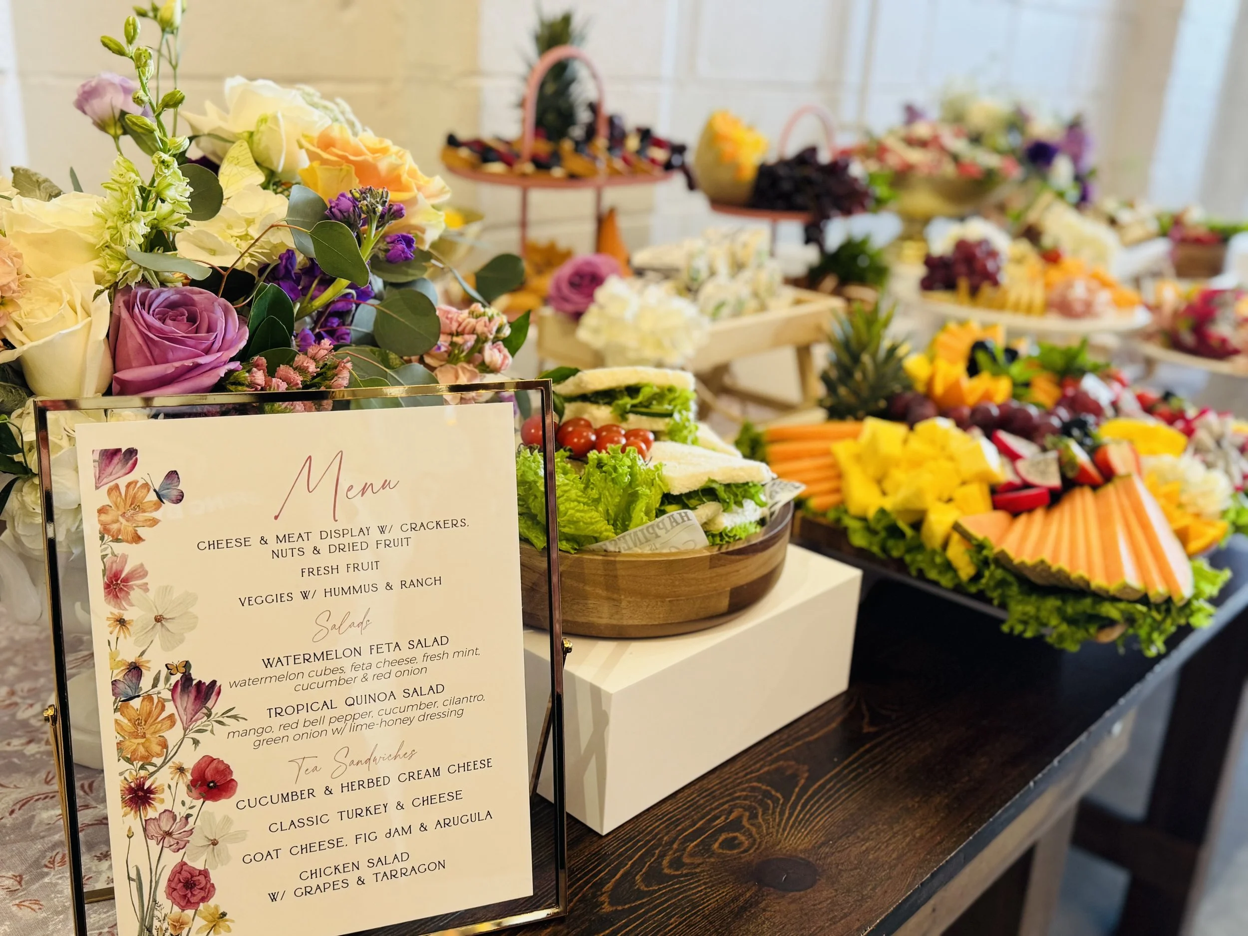 Display of various food items, including cheese and meat, arranged on tables, with a menu in the foreground listing different salads and sandwiches, and blurred background with additional food displays.