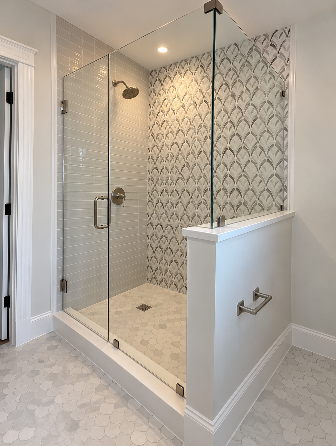 Custom walk-in shower with frameless glass enclosure, decorative mosaic accent wall, gray subway tile, and white scalloped tile flooring.