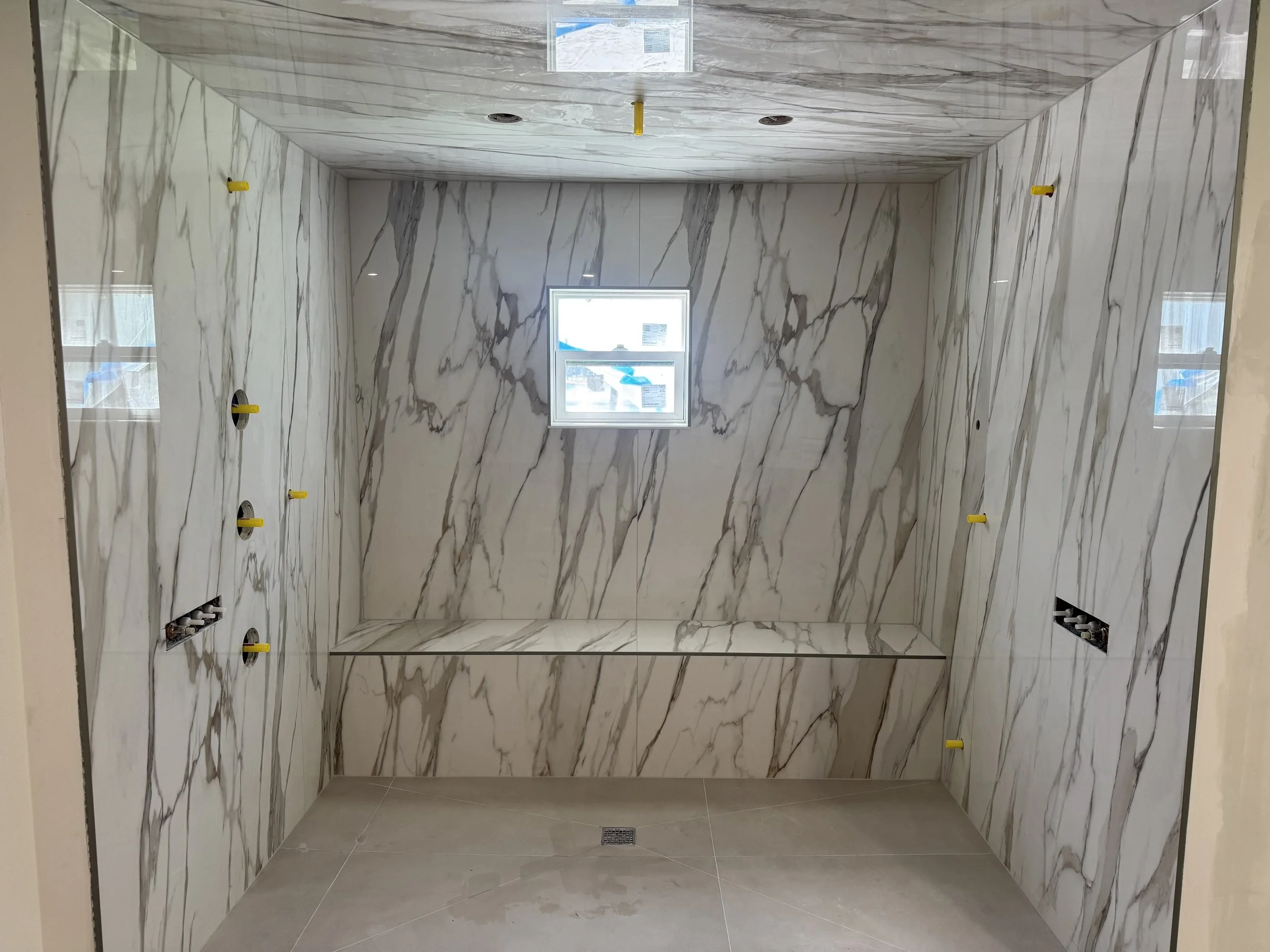Custom walk-in shower featuring large-format white marble-look tile with gray veining, a built-in shower niche, and matching tiled ceiling.