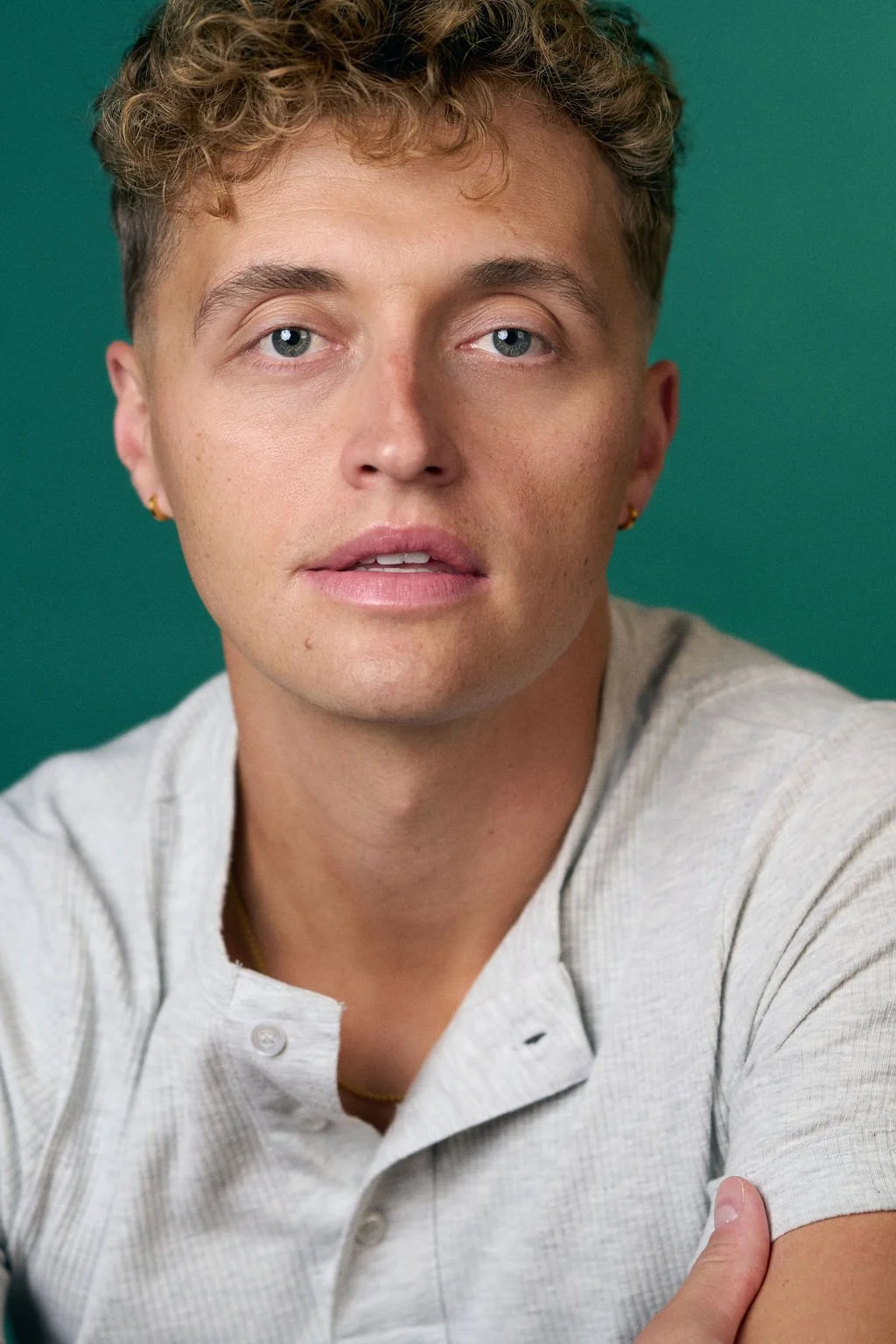 Close-up portrait of a young man with curly brown hair wearing a light shirt against a teal background