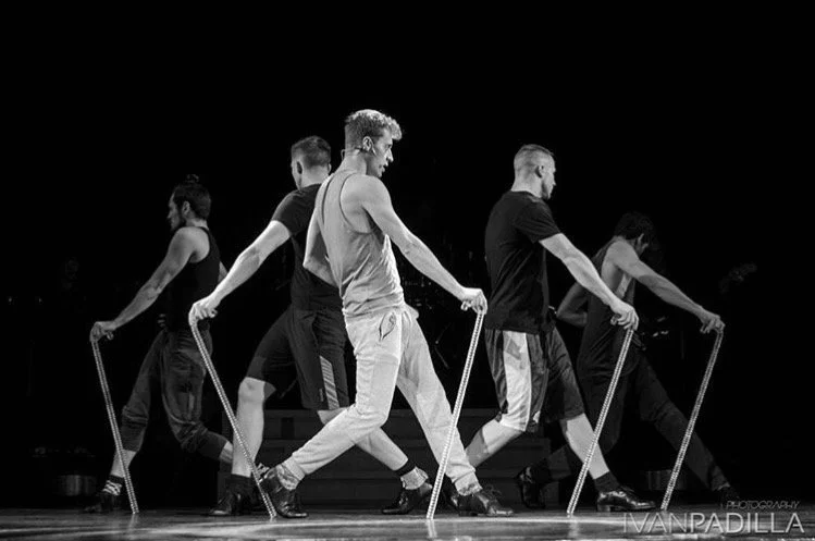 Black-and-white stage performance featuring five dancers walking in formation with ropes.