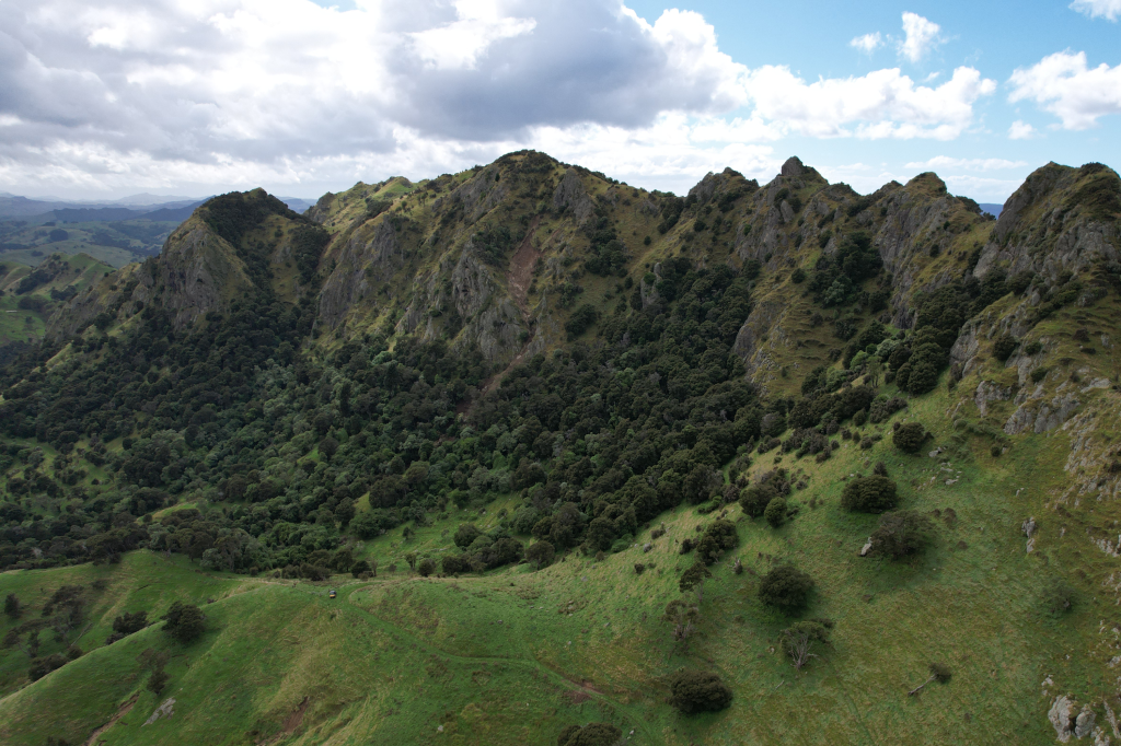 Mountains with lush green vegetation and scattered trees under a partly cloudy sky.